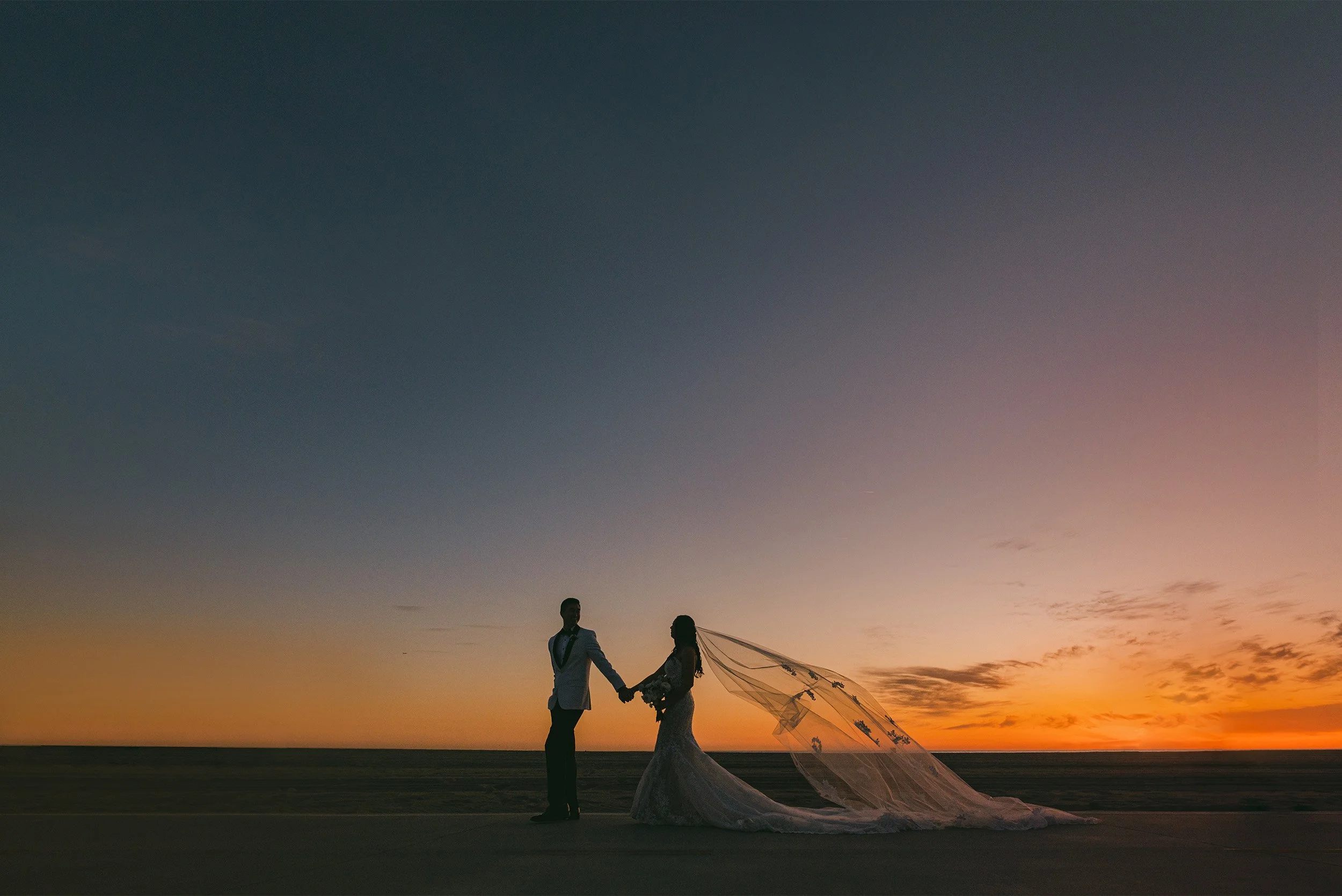 Santa Monica wedding photographer captures dramatic sunset silhouette of bride and groom with veil flowing against orange sky at the Proper Hotel