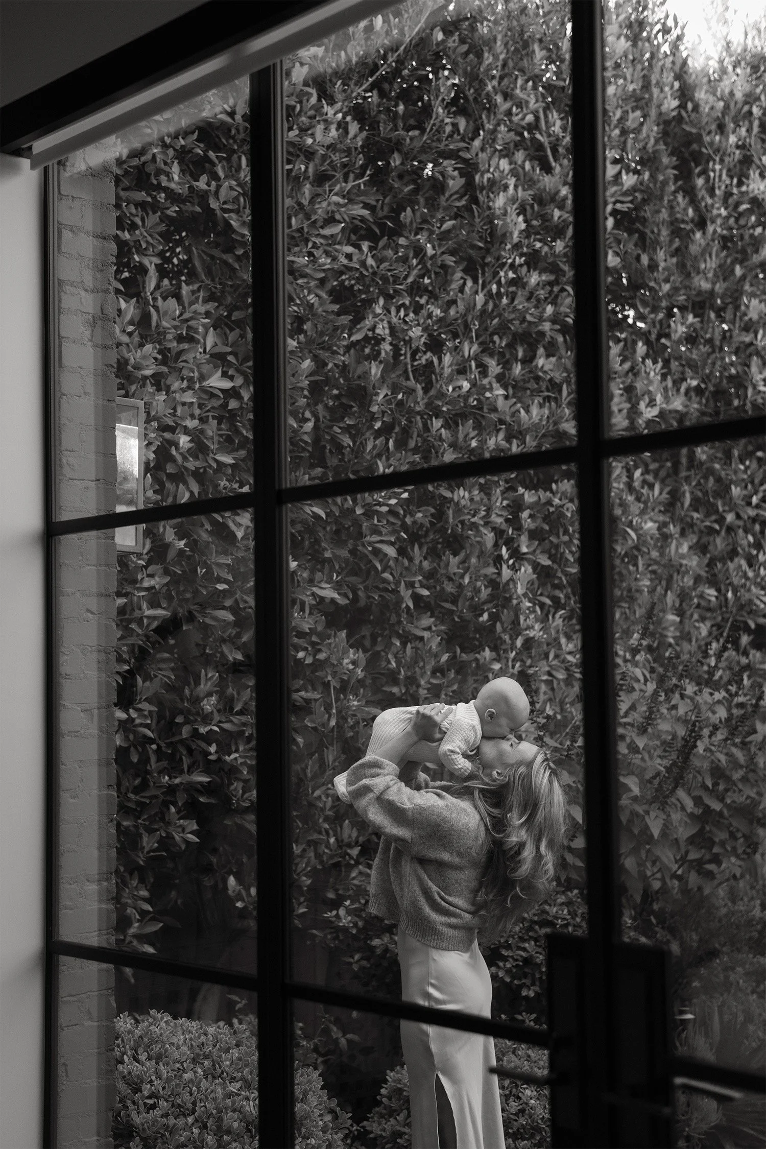 Orange County family photographer captures mother lifting baby up through a garden window reflection