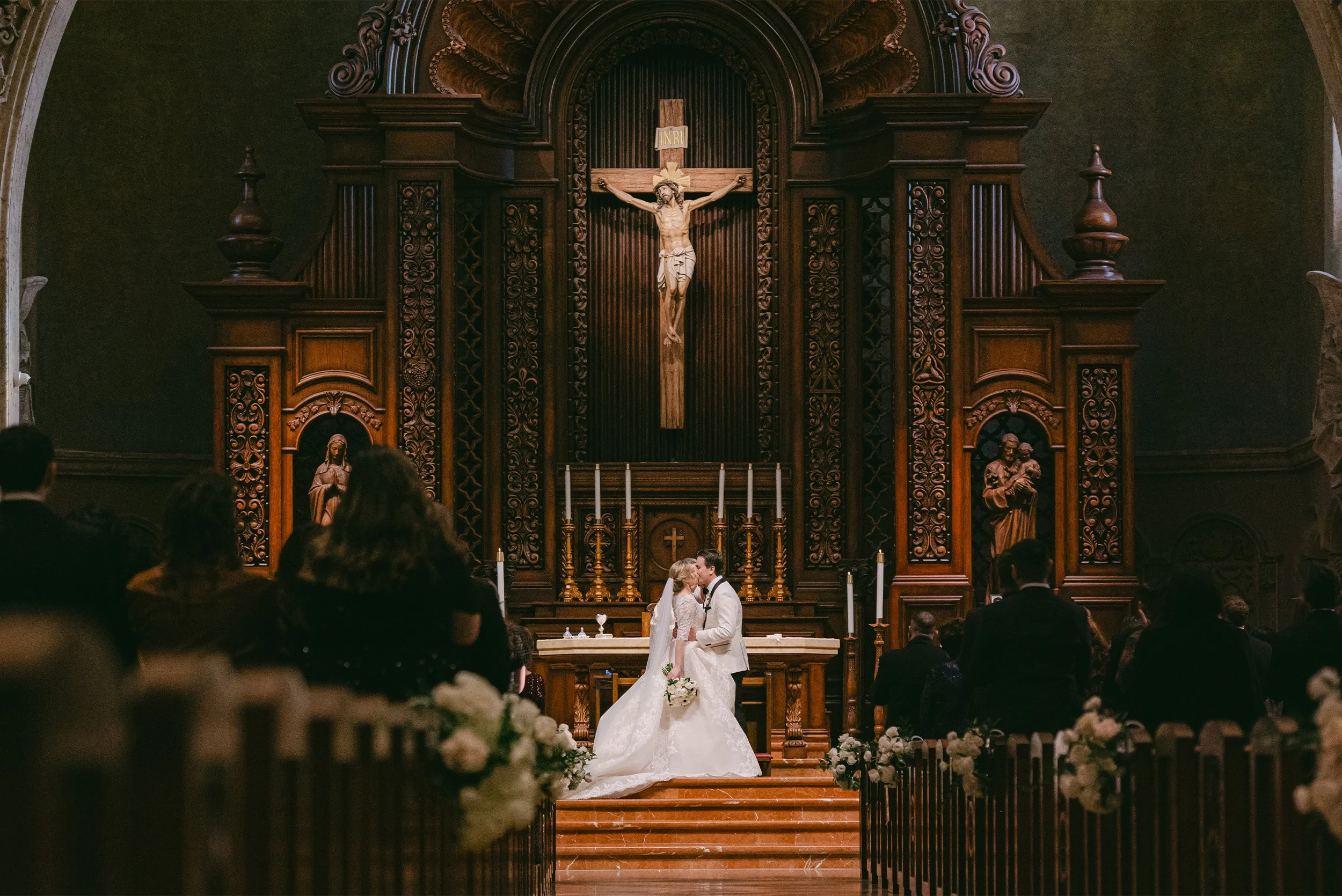 Award-winning wedding photographer in Orange County captures couple's first kiss at ornate church altar beneath wooden crucifix