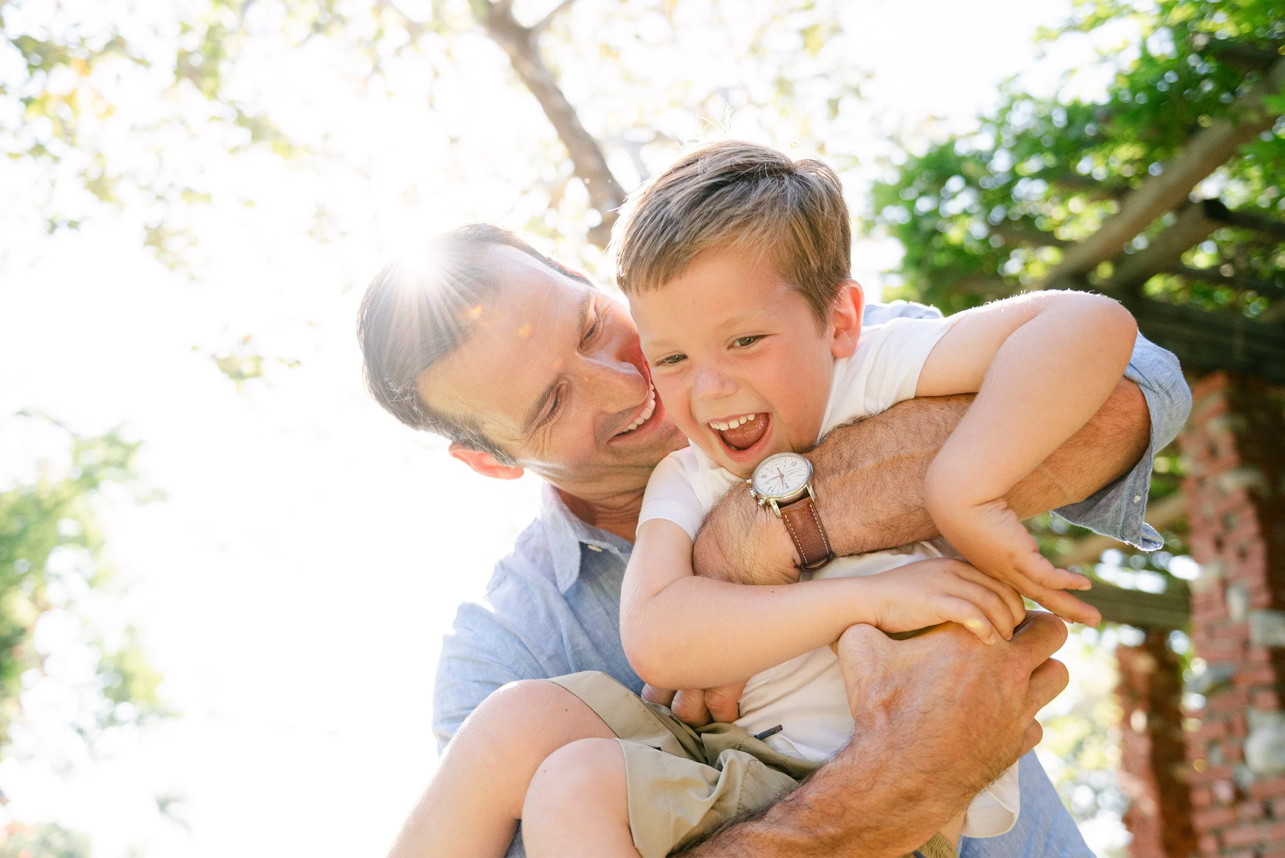Highly recommended family photographer in Orange County captures joyful father-son moment in dappled sunlight
