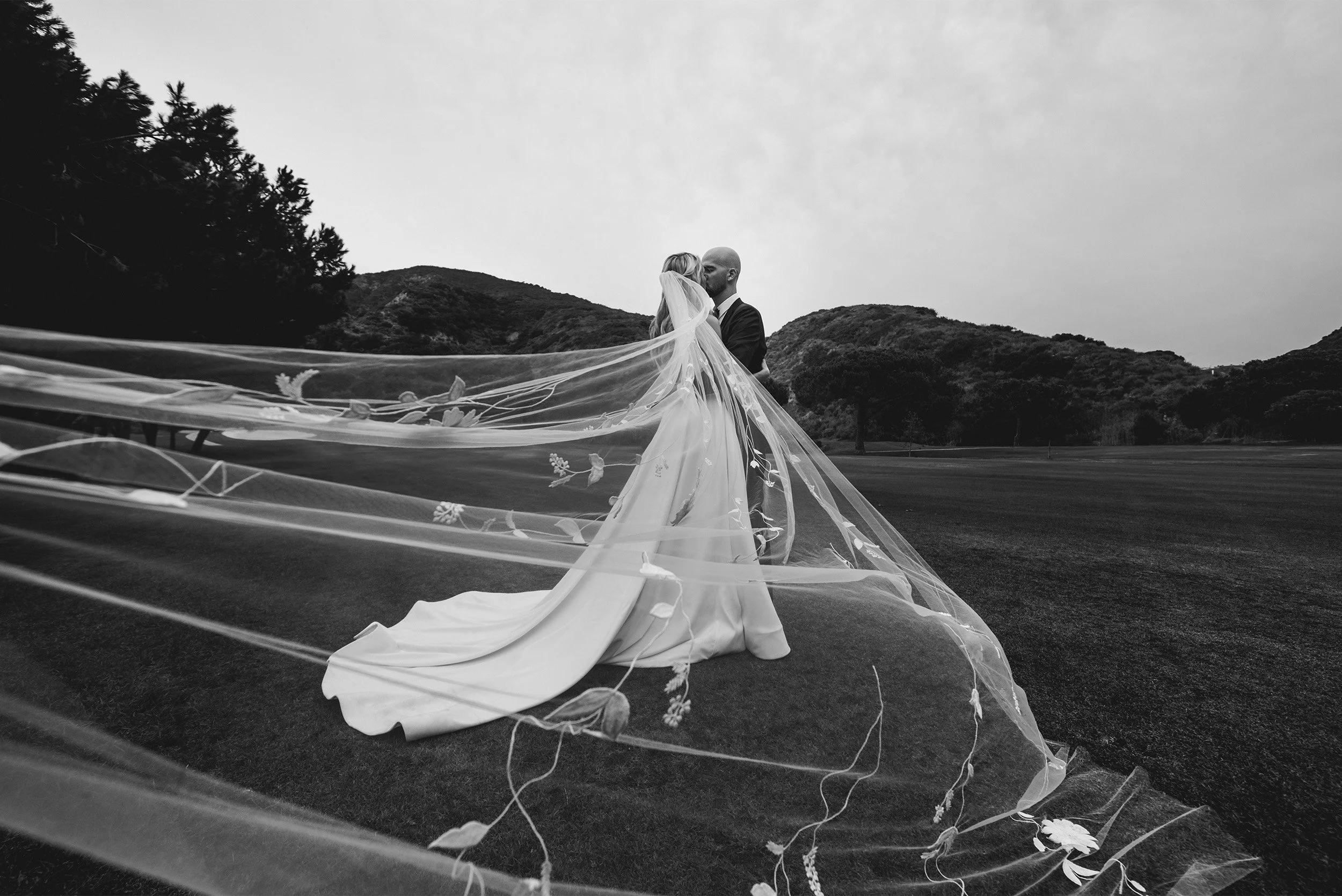 Highly recommended wedding photographer in Orange County captures bride and groom kissing on The Ranch at Laguna Beach golf course hillside with dramatic flowing veil, black and white