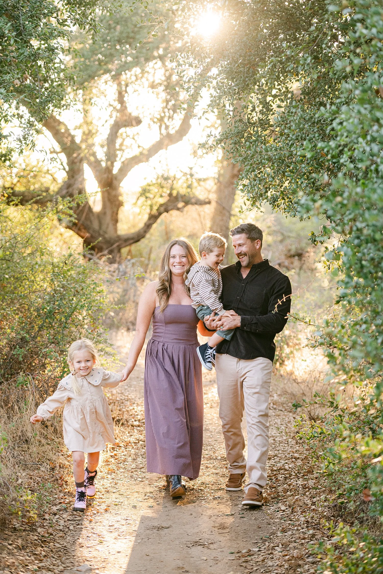 Family of four walking together on a sunlit oak-lined trail, Award-winning family photographer in Orange County
