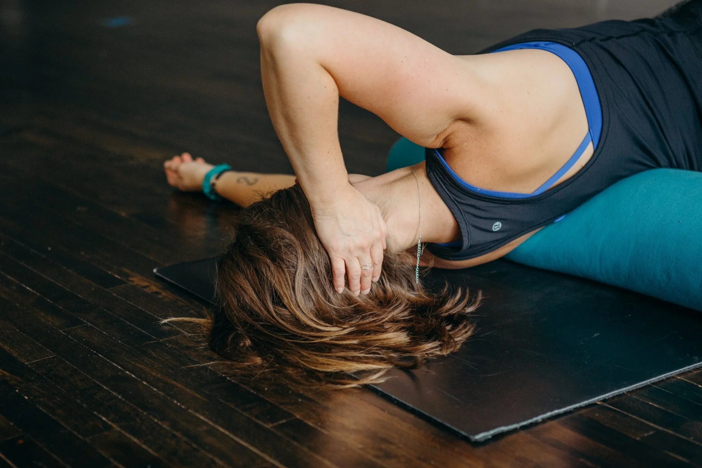 Person lying on a yoga mat performing a stretching exercise with head and arm on a bolster.