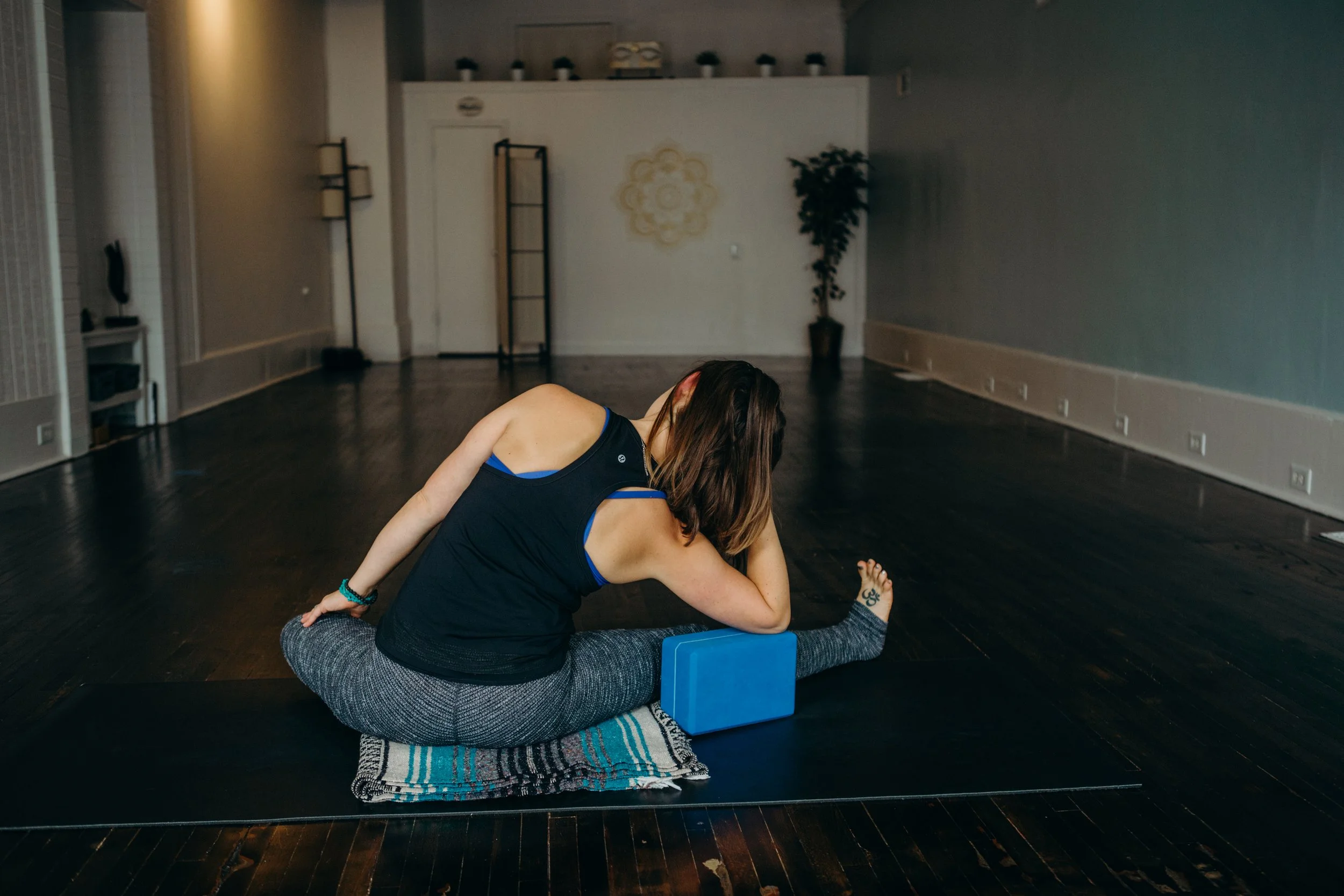 Person practicing yoga in a studio, sitting on a mat with a blanket and using a yoga block.
