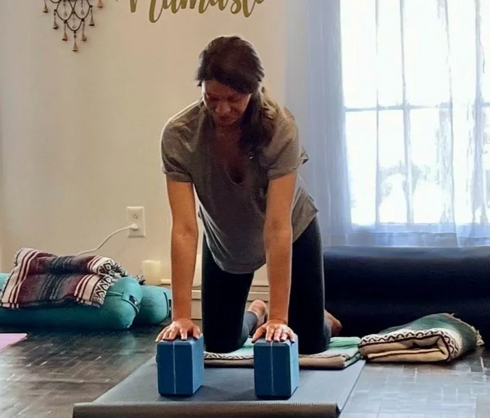 Woman practicing yoga with blocks on mat in room with blankets and cushions