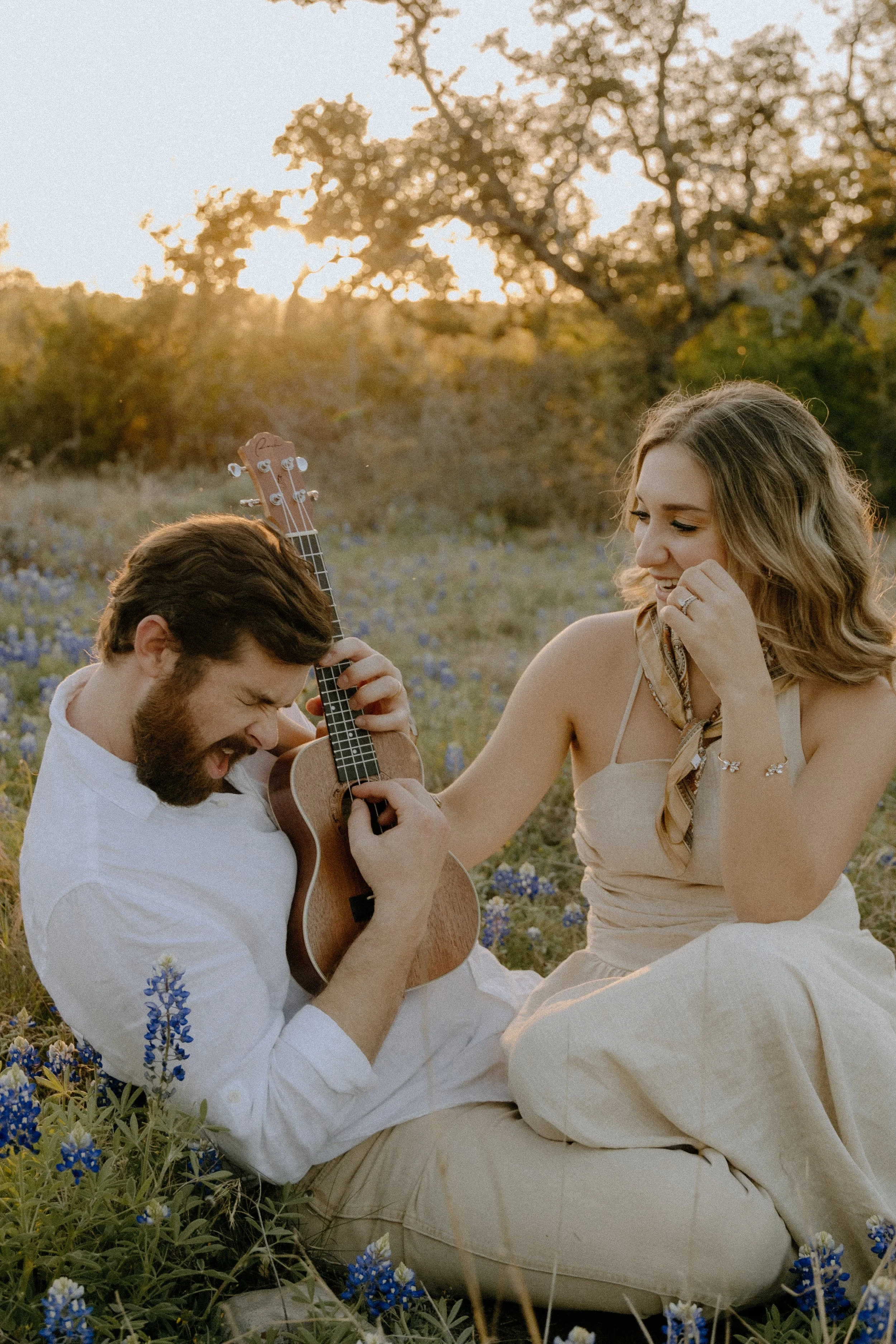 Houston & Texas Family, Couples, Newborn, Maternity, Bridal Photography – Couple laughing while strumming guitar in Austin TX meadow.