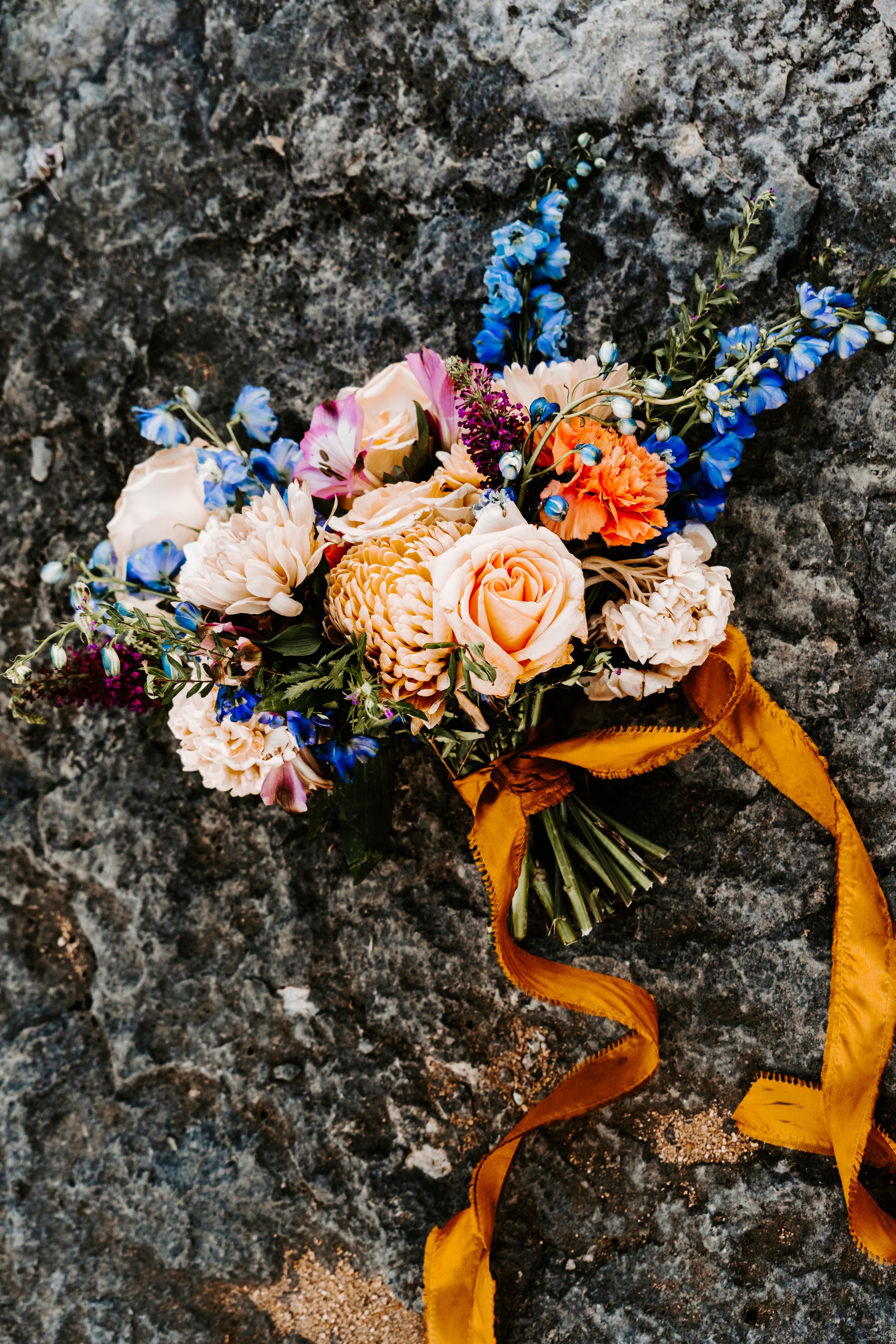 Wedding & Elopement Photography, Blue and orange floral bouquet displayed on a rocky surface.