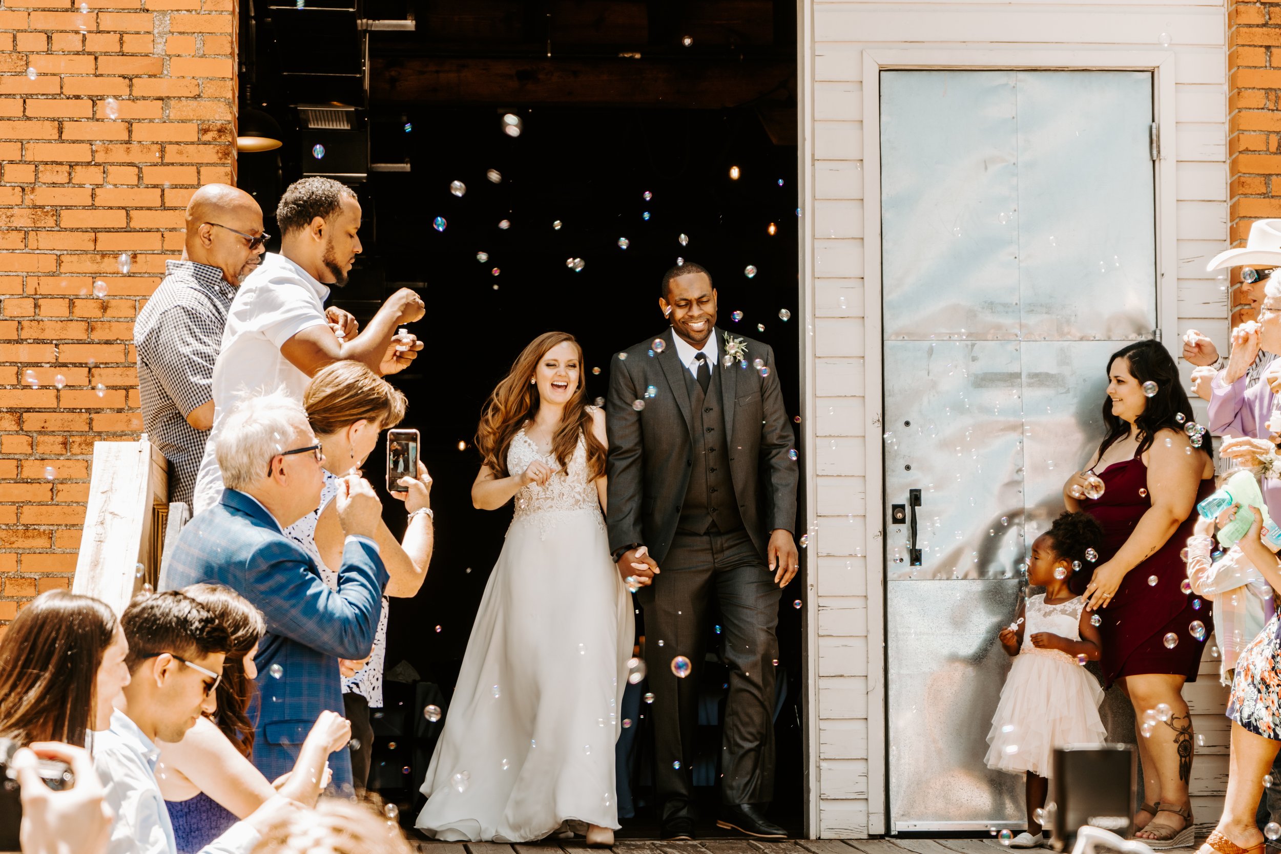 Wedding & Elopement Photography,
Newlyweds exiting building while guests blow celebration bubbles.