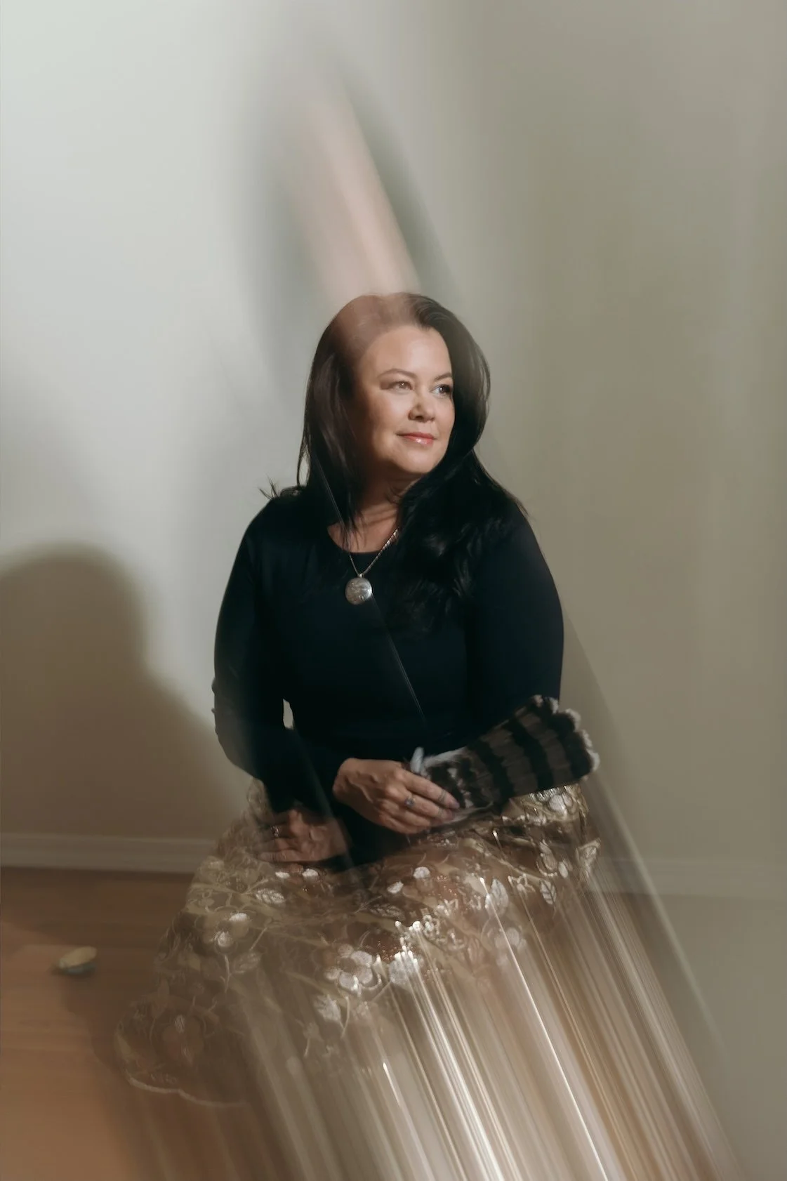 Danielle Searancke, Indigenous Medium, sitting with gold skirt and holding owl feathers.