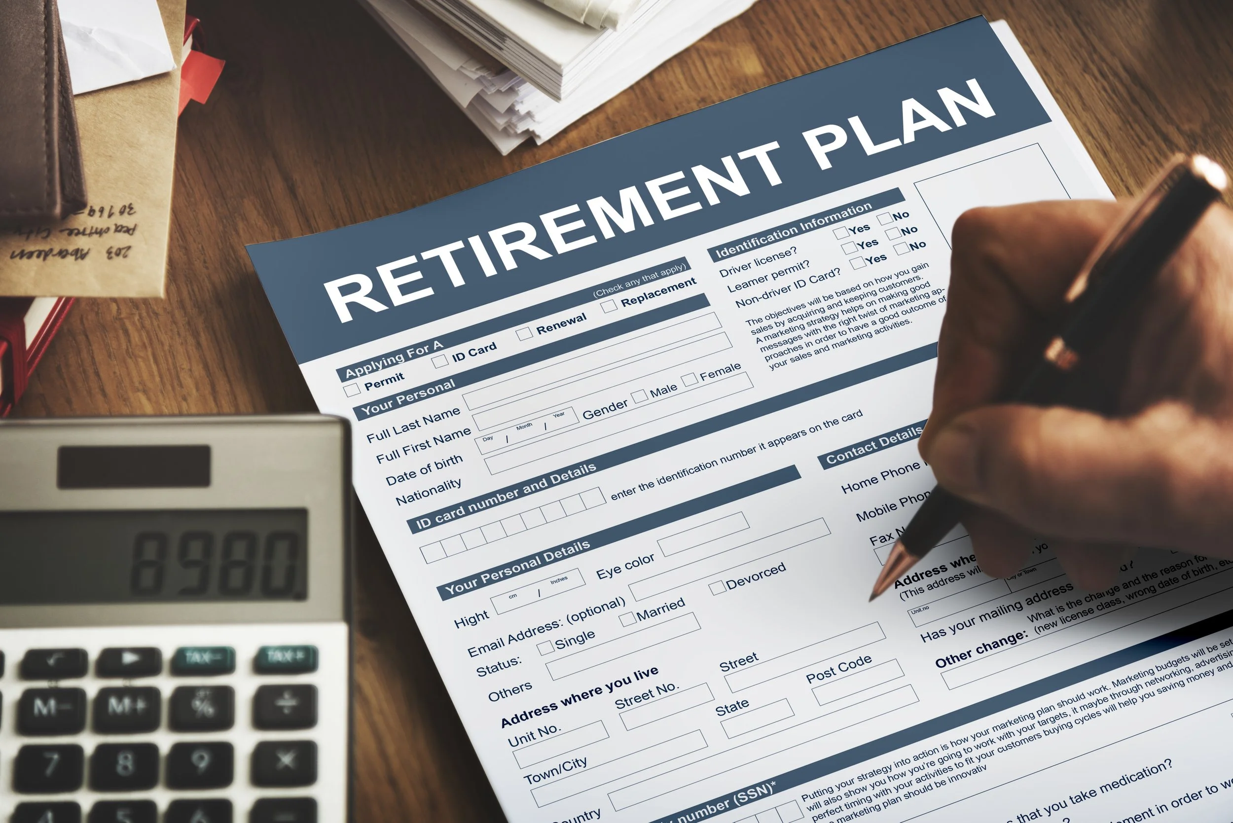 A person filling out a retirement plan form on a wooden desk with a calculator nearby.