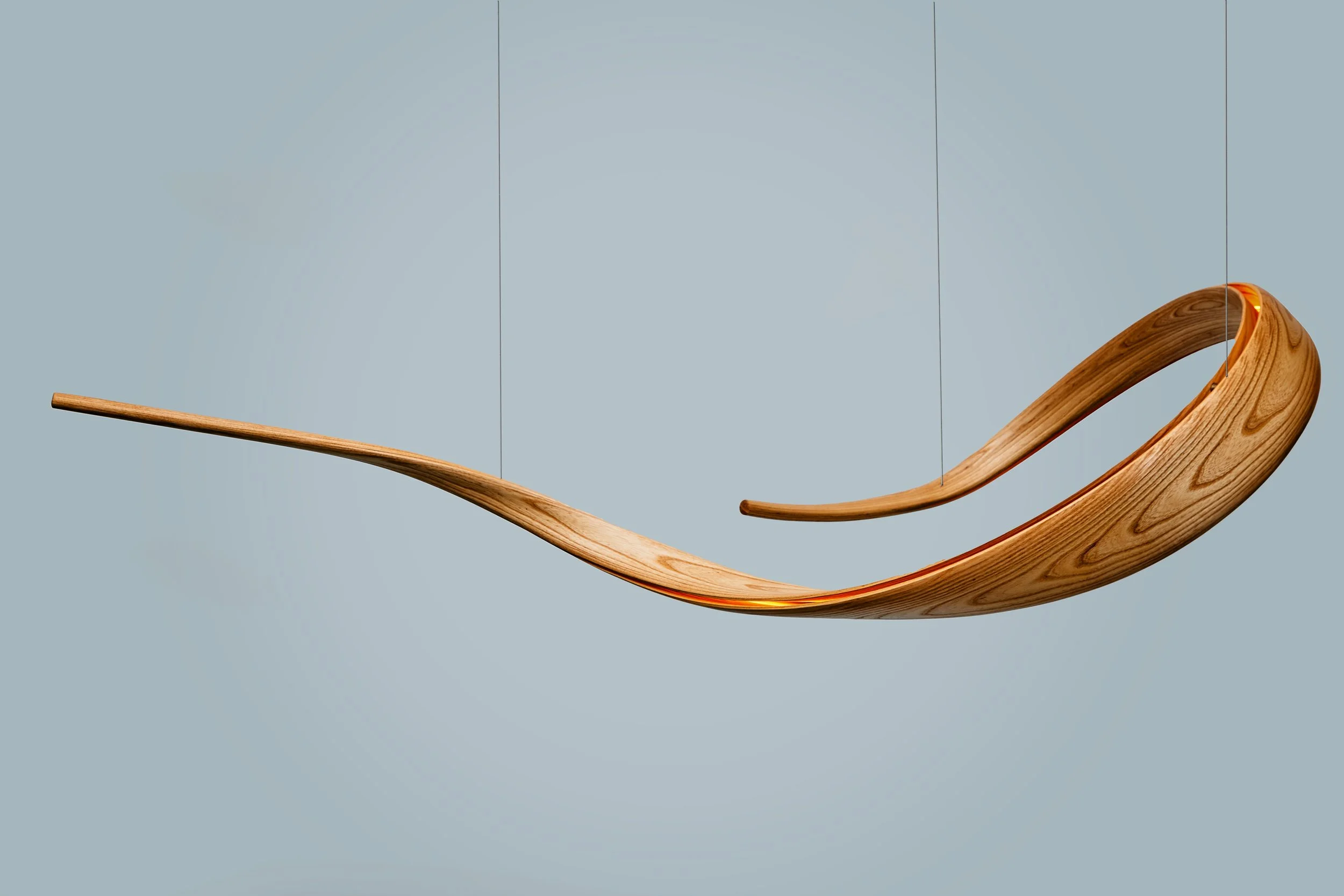 Illuminated bent wood lighting sculpture with suspended flowing curved form.