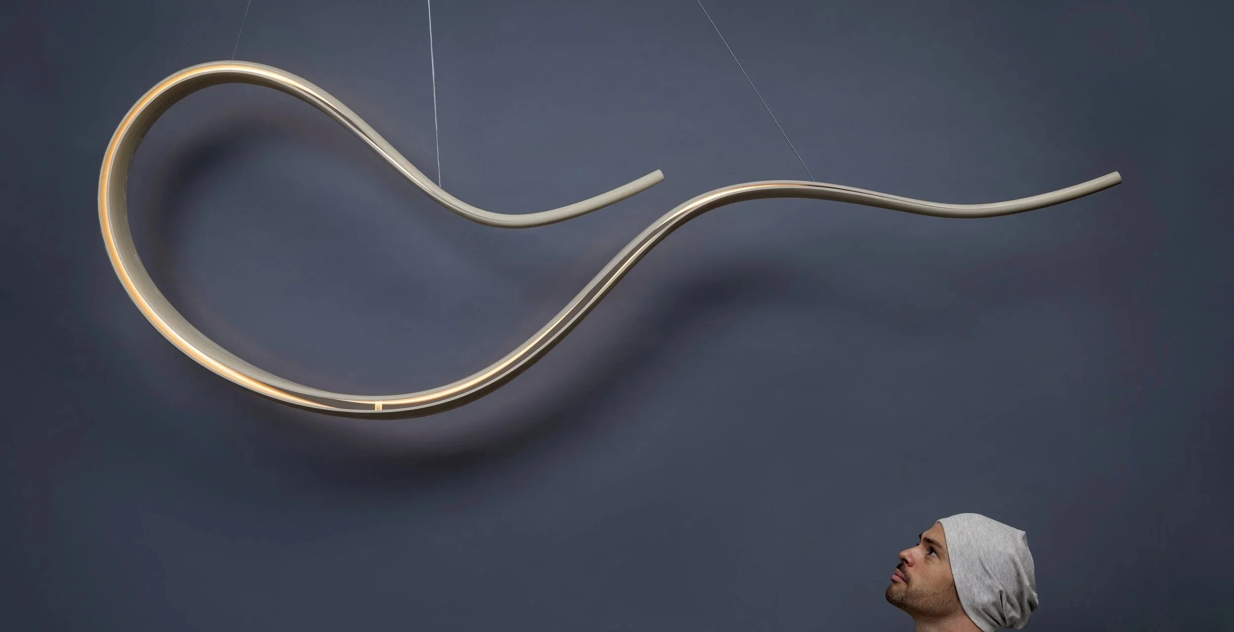 Large suspended sculptural design piece by Adam Bentz featuring flowing illuminated ribbon forms in a minimalist architectural composition.