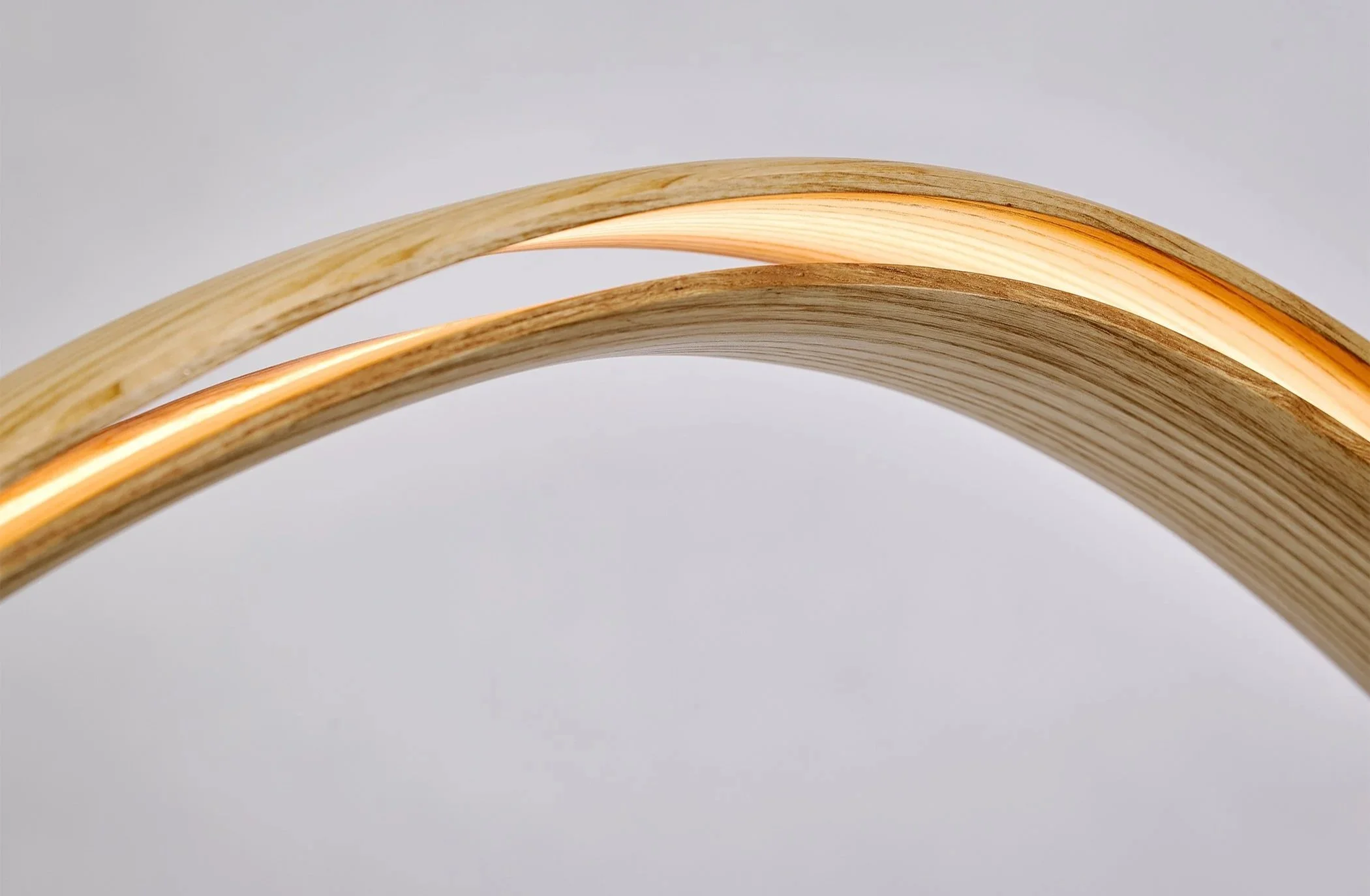 Detail of bent wood sculptural lighting with illuminated edge and layered wood grain.