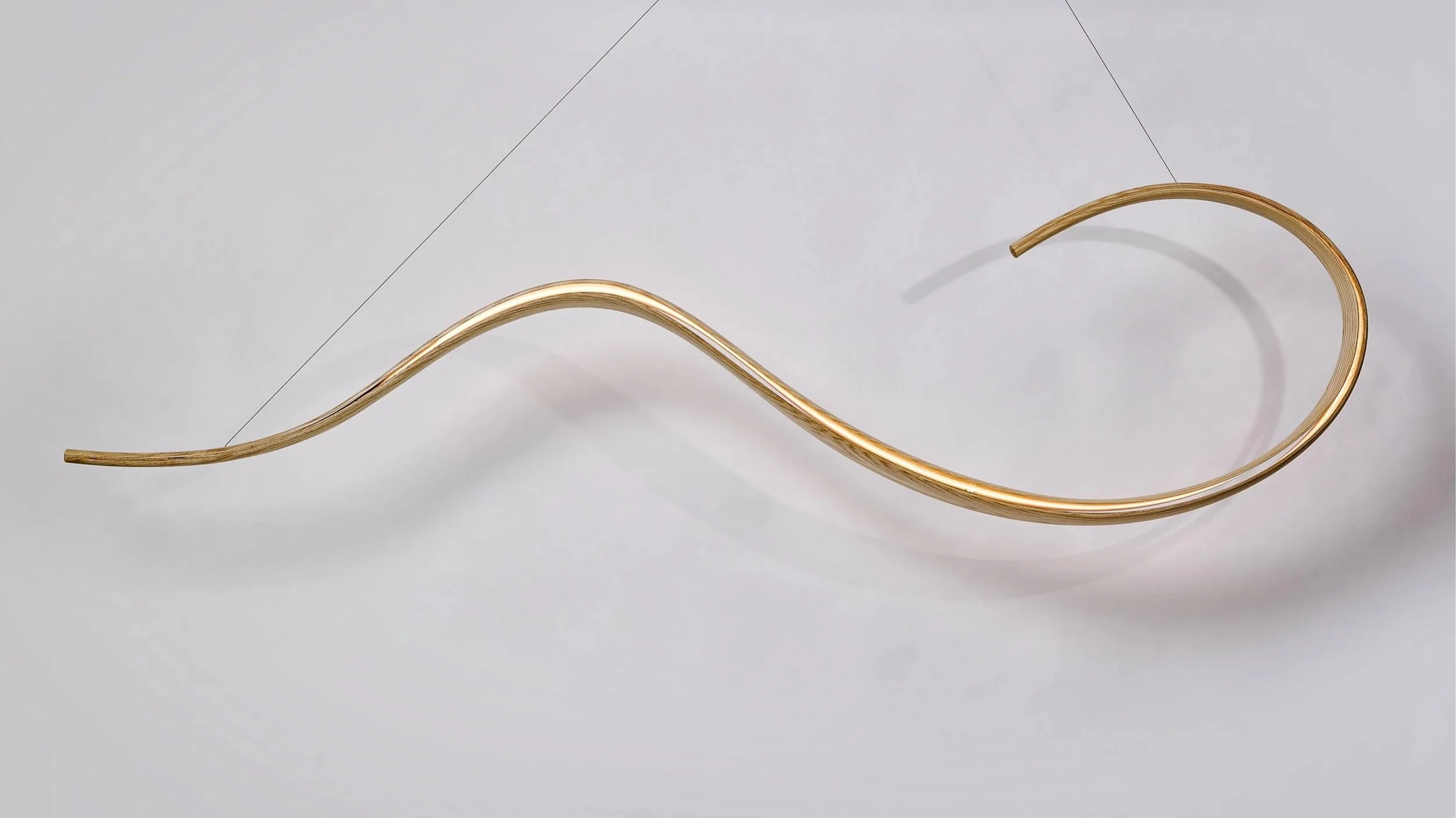 Suspended bent wood sculptural lighting with flowing illuminated curve.