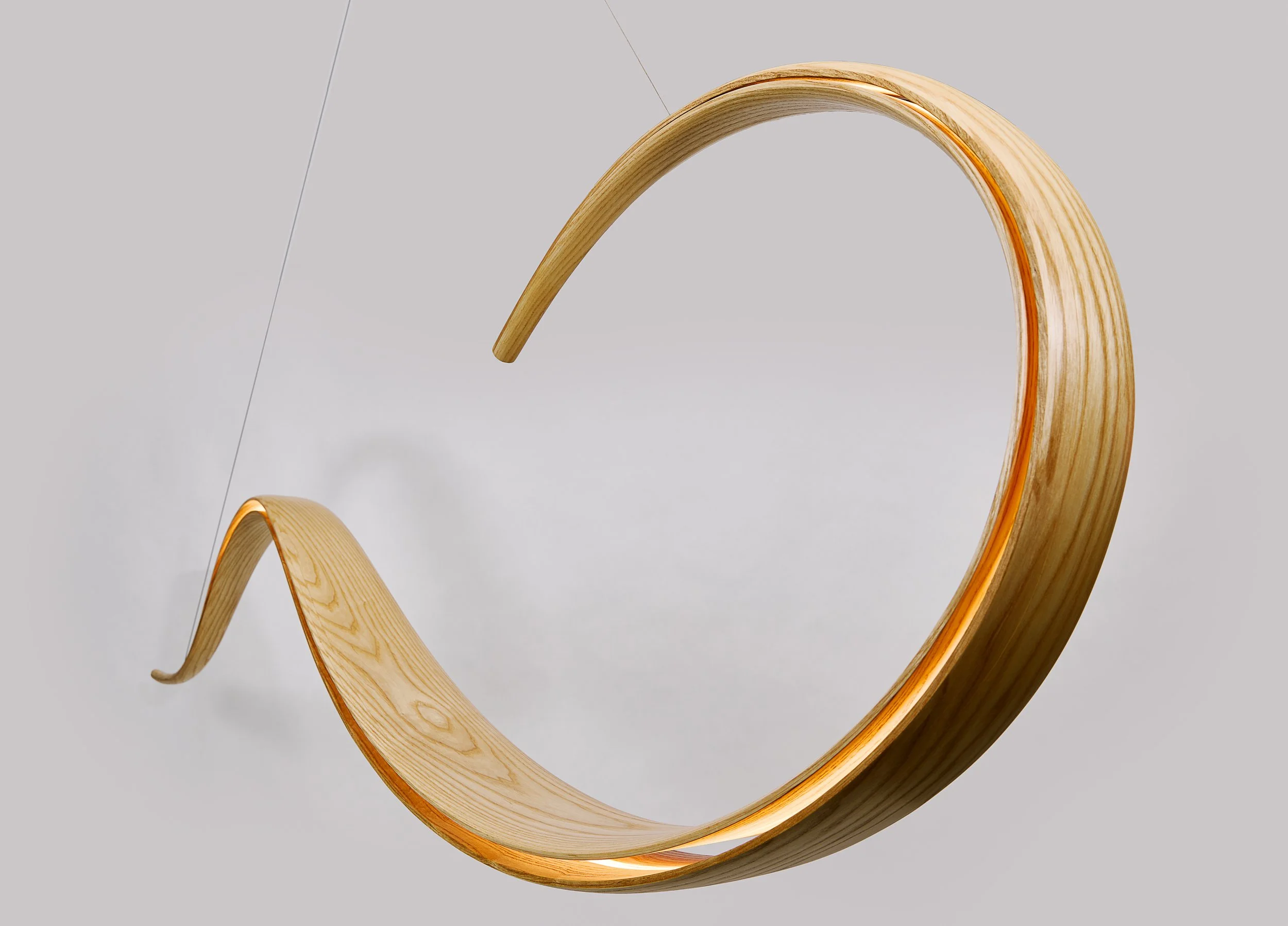 Suspended bent wood lighting sculpture with curved illuminated form.