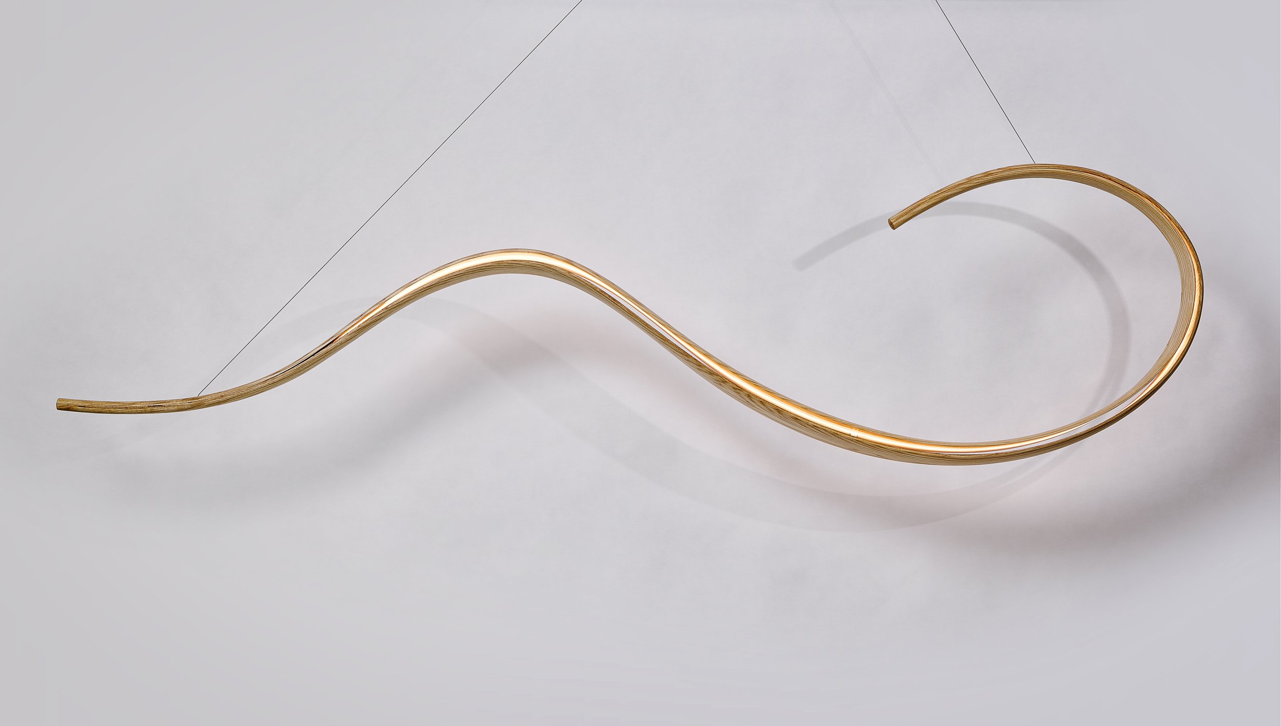 Suspended sculptural lighting by Adam Bentz featuring an illuminated curved wood form.