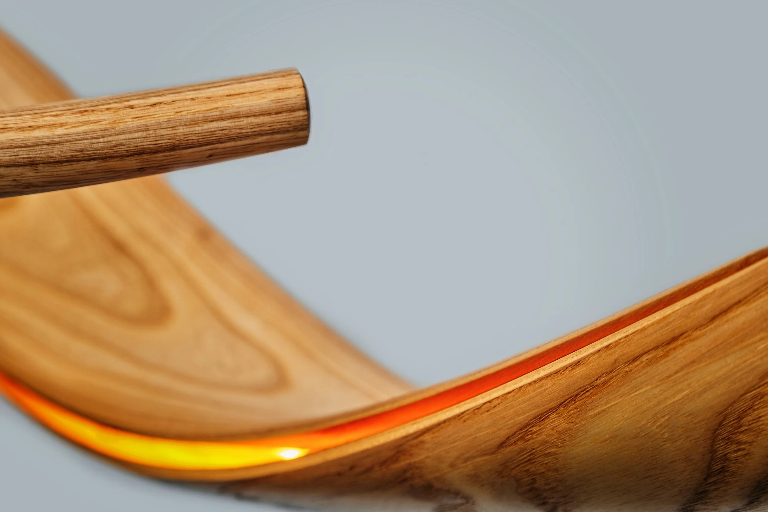Suspended bent wood sculptural lighting installation with illuminated flowing organic form.