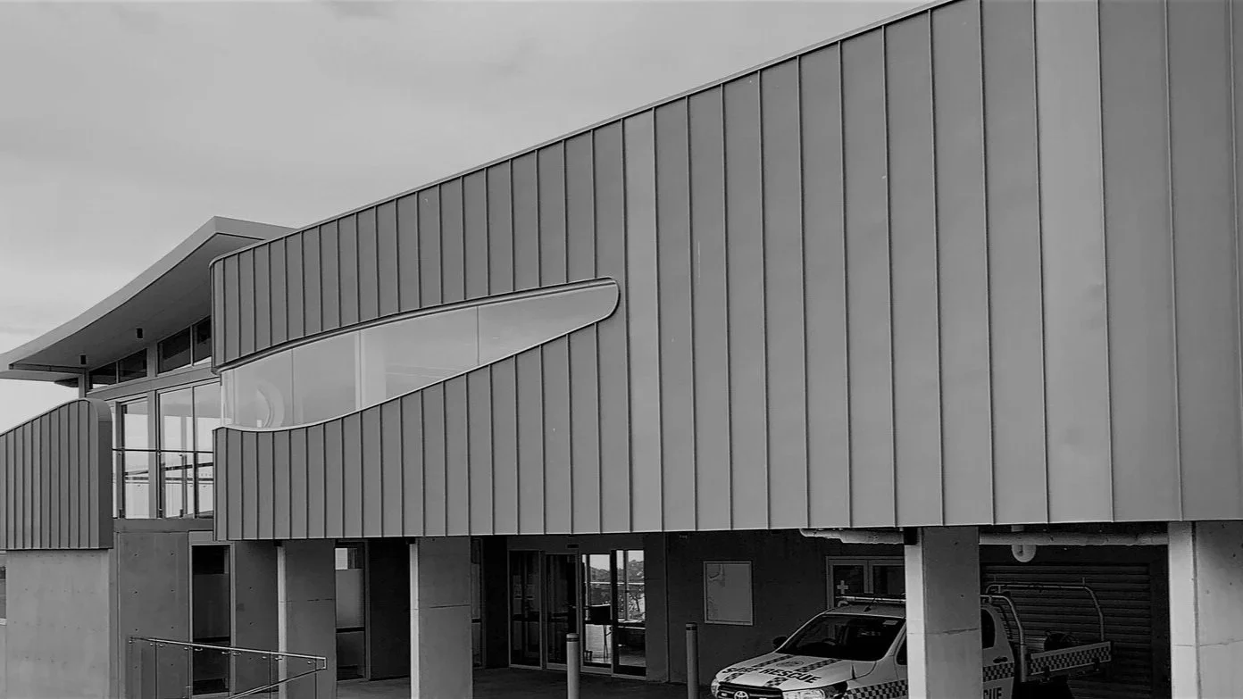 Modern building with curved metal exterior, glass windows, and a police vehicle parked underneath.