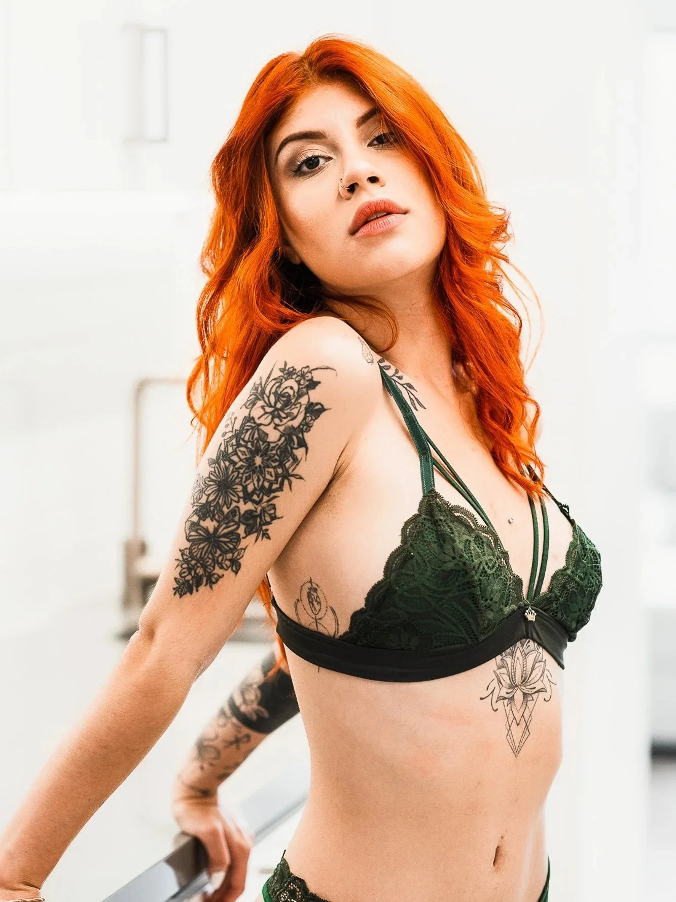 A woman with long red hair and tattoos wearing a green lace bra.