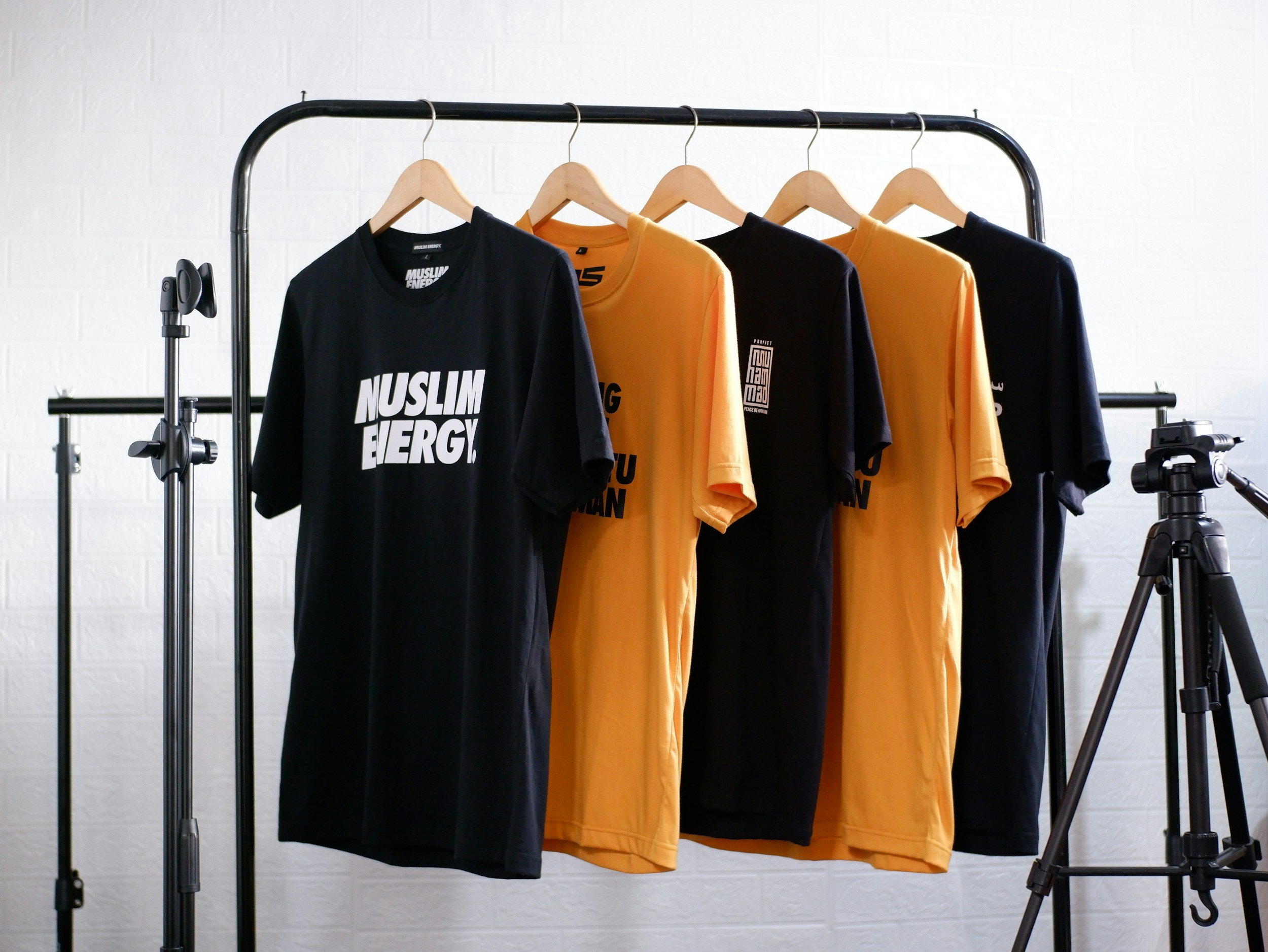 Black and yellow T-shirts hanging on a clothing rack inside a studio with tripods visible on either side.