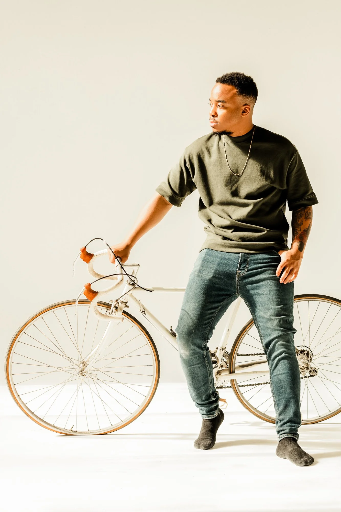 Full-body portrait of Khalif standing beside a vintage-style bicycle in a bright studio with soft light.