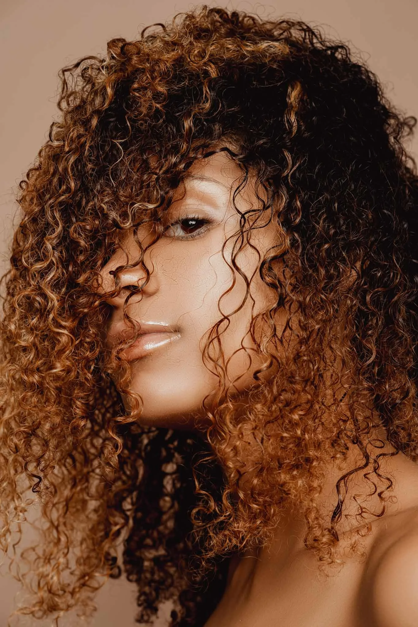 Close-up portrait of a woman with curly hair partially covering her face, looking confidently at the camera.