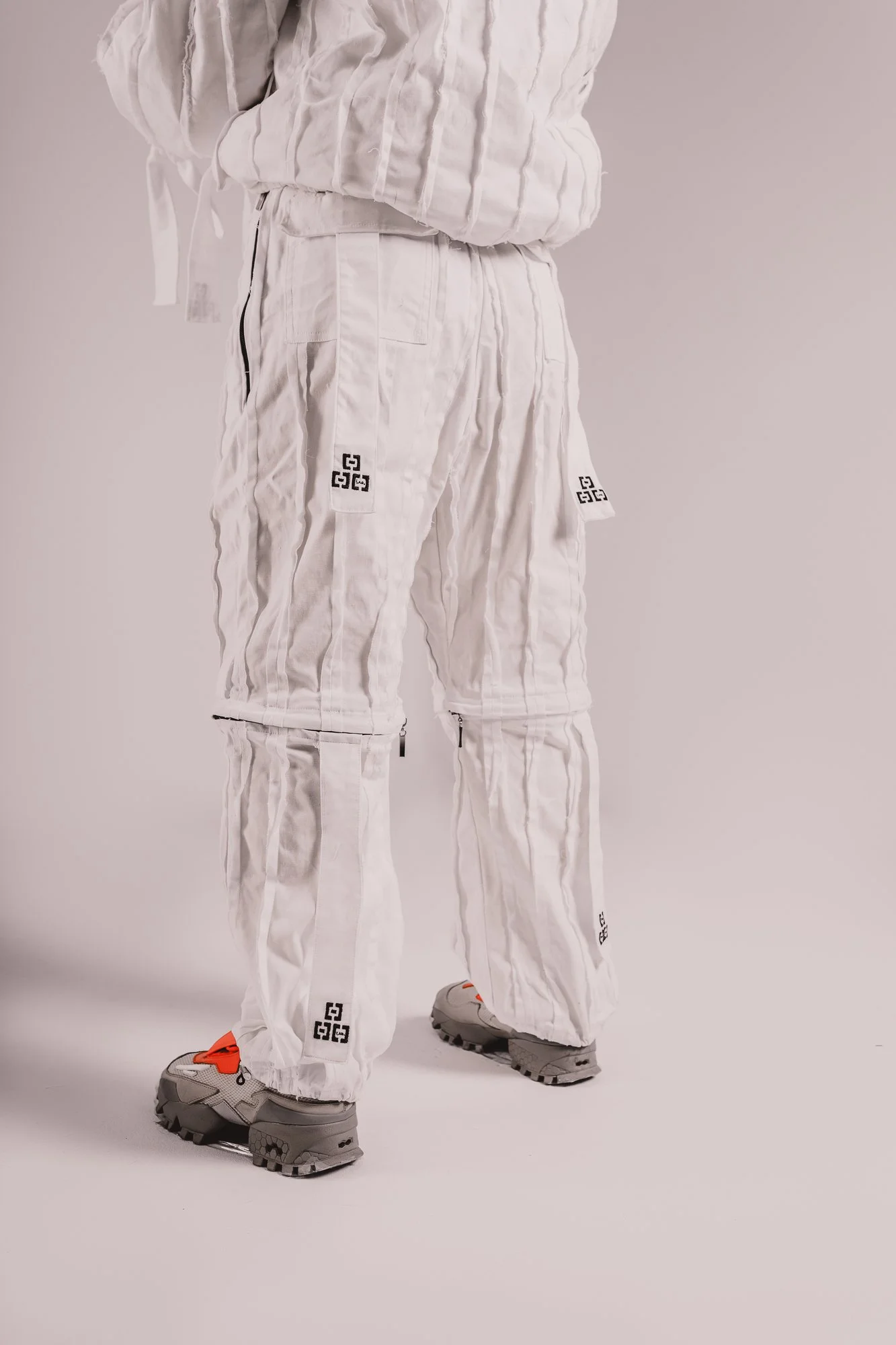 Person wearing white athletic pants, a matching top, and gray sneakers with orange accents, standing against a plain background.