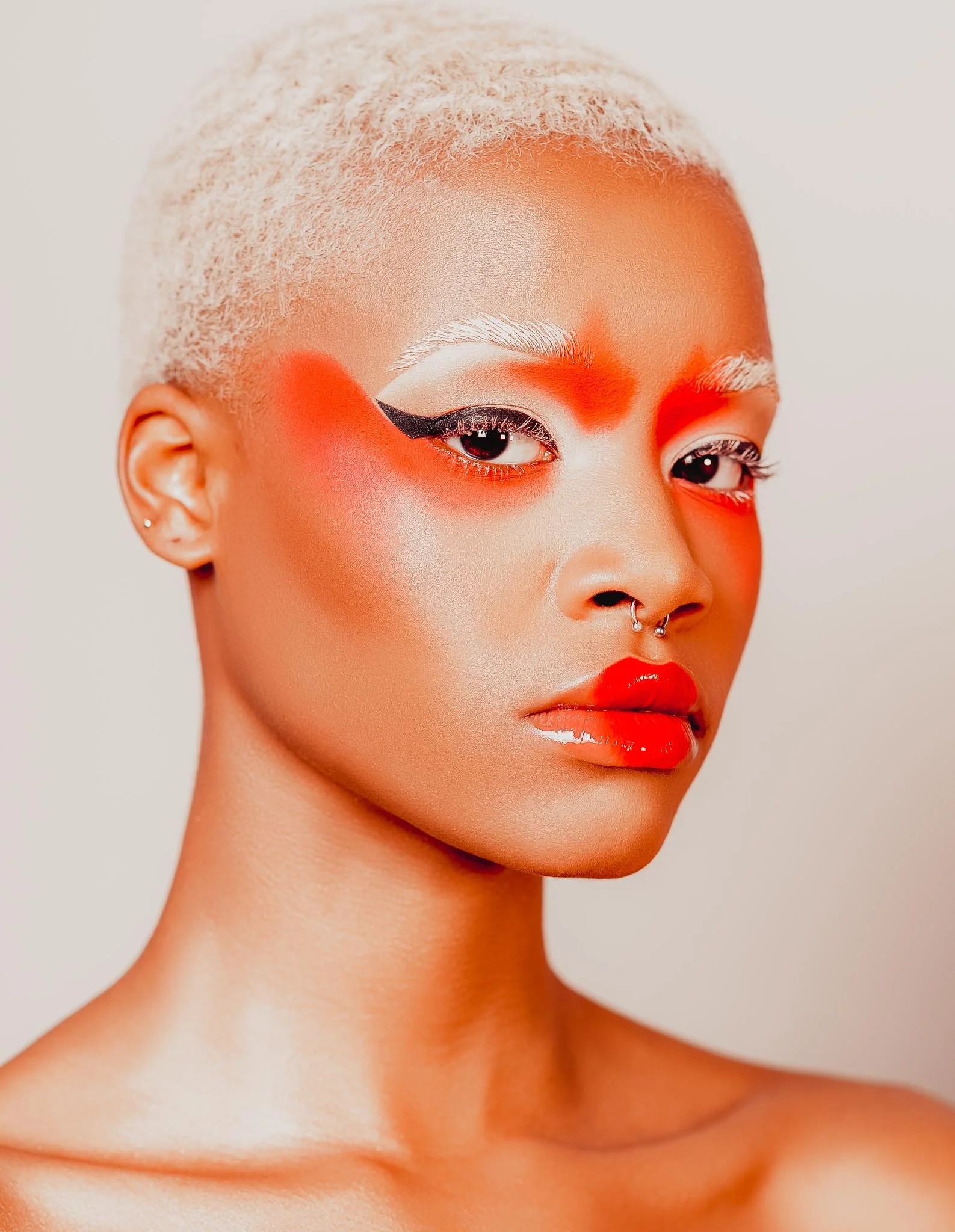 A woman with platinum blonde hair and bold makeup featuring red and white eye makeup, orange blush, and bright red lipstick.