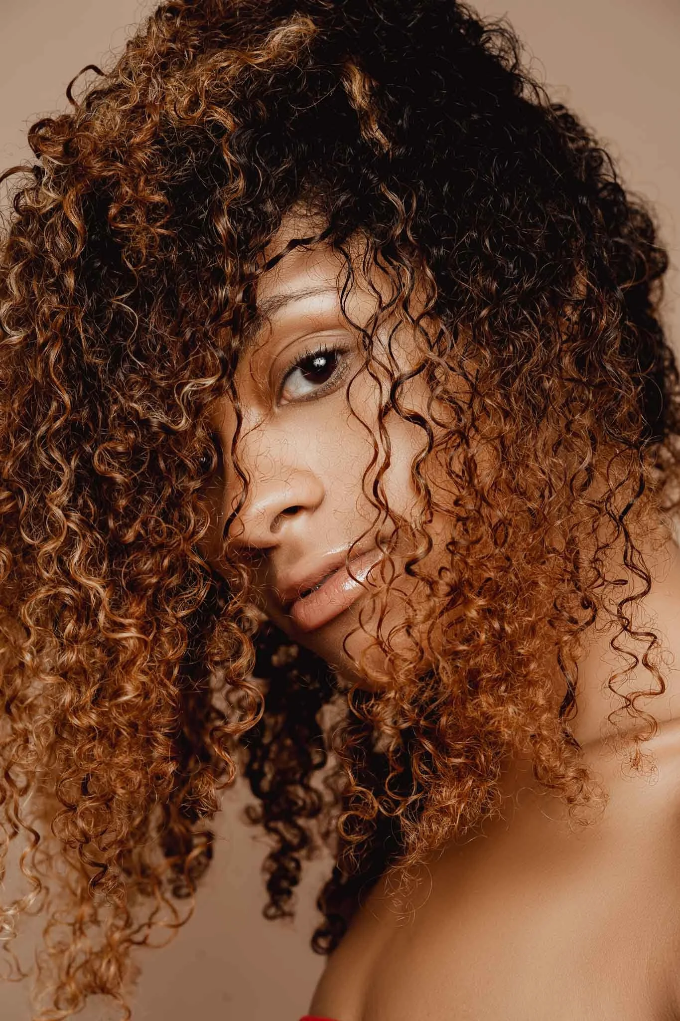 Close-up portrait of a woman with curly hair, partially covering her face, looking into the camera.