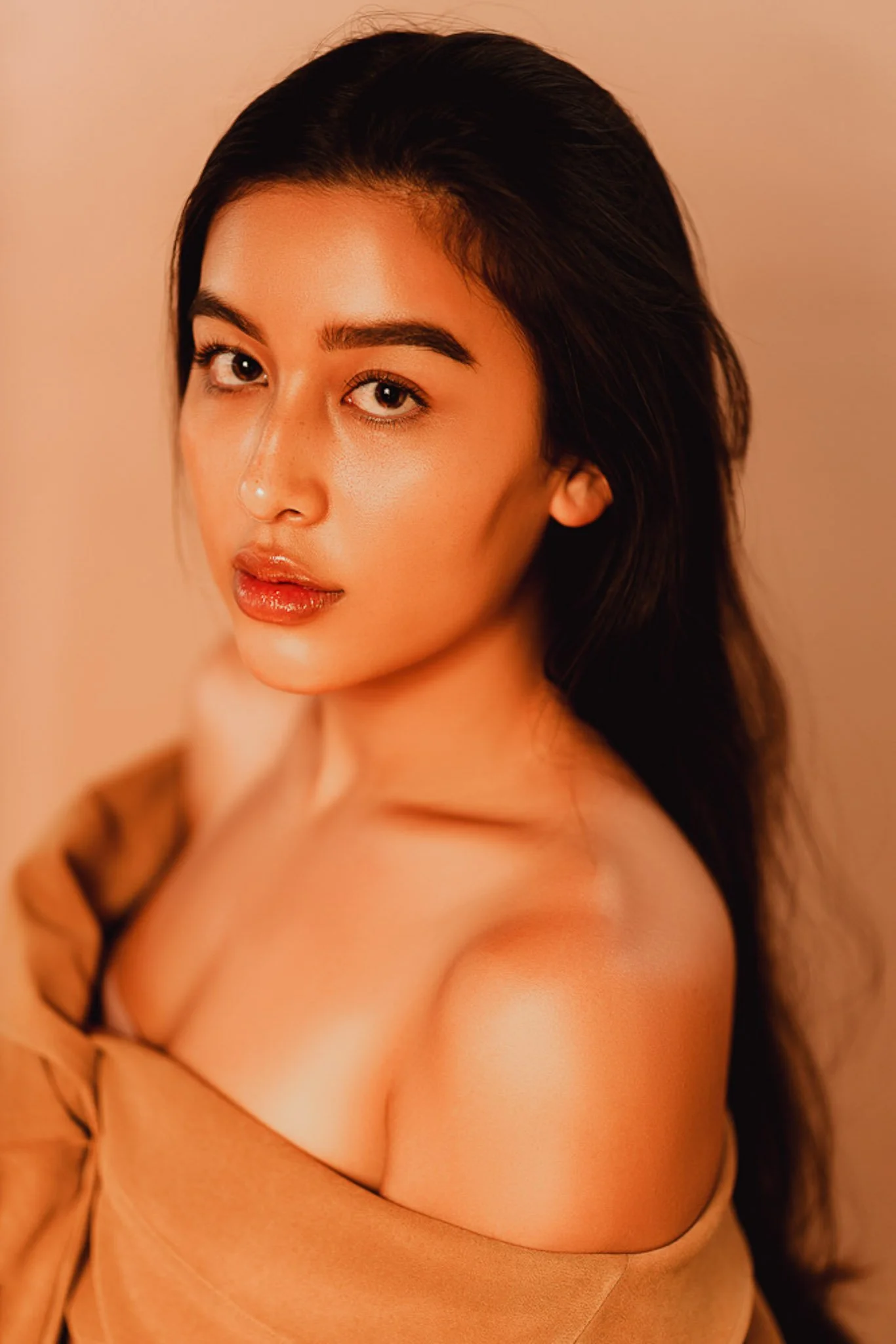 A young woman with long dark hair, light skin, brown eyes, glasses, with a serious expression, wearing a brown off-shoulder top.