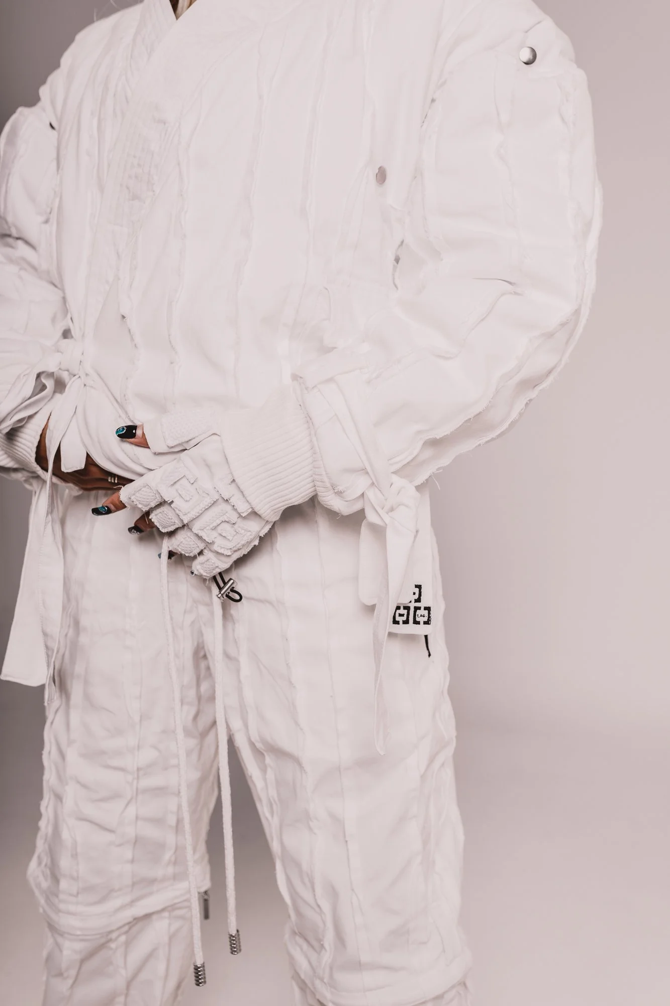 Close-up of a person wearing a white combat-style outfit, including a padded jacket and matching pants, with their arms crossed.