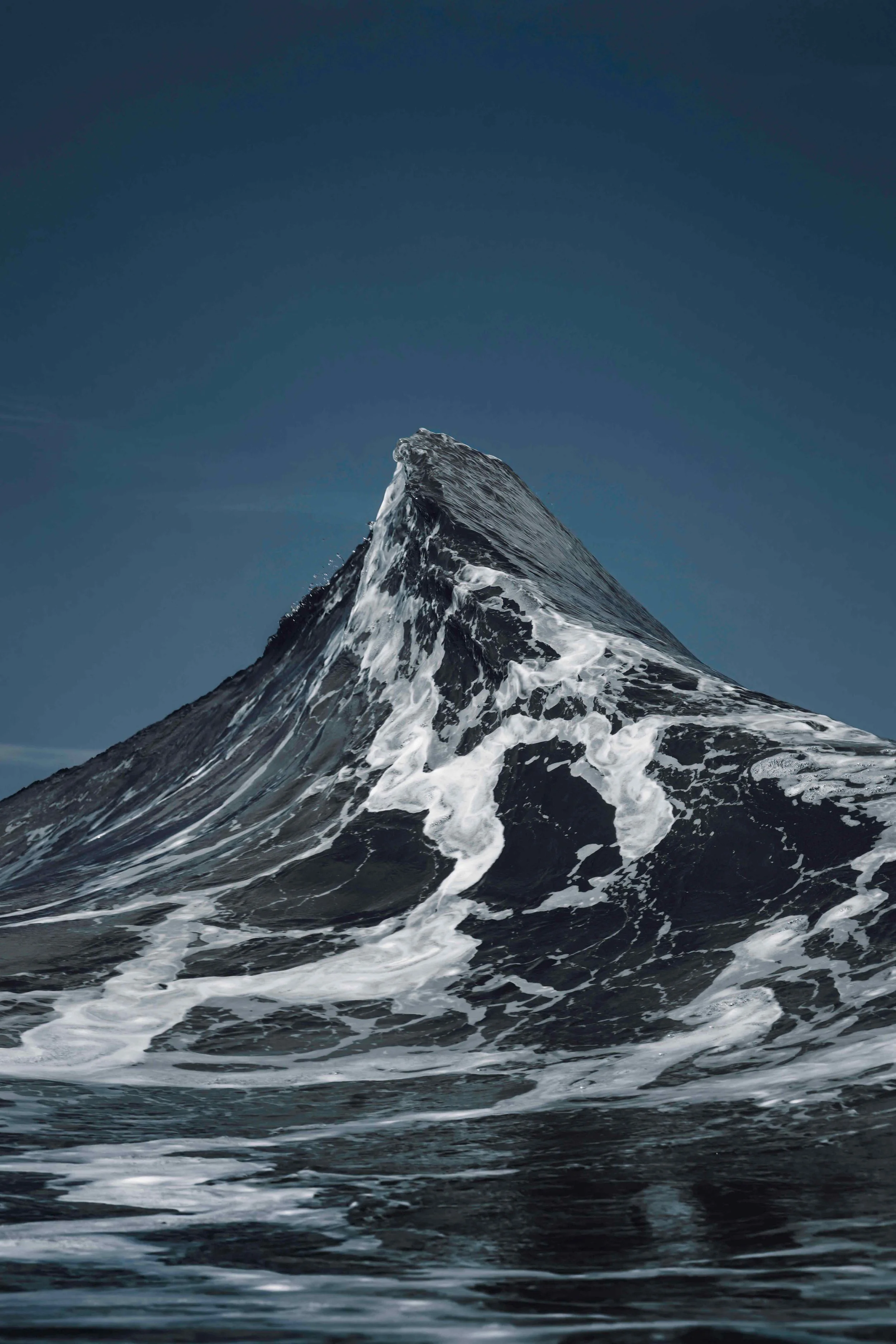 Two ocean waves crashing together forming a peak shape resembling the Matterhorn mountain, captured in dramatic coastal light.