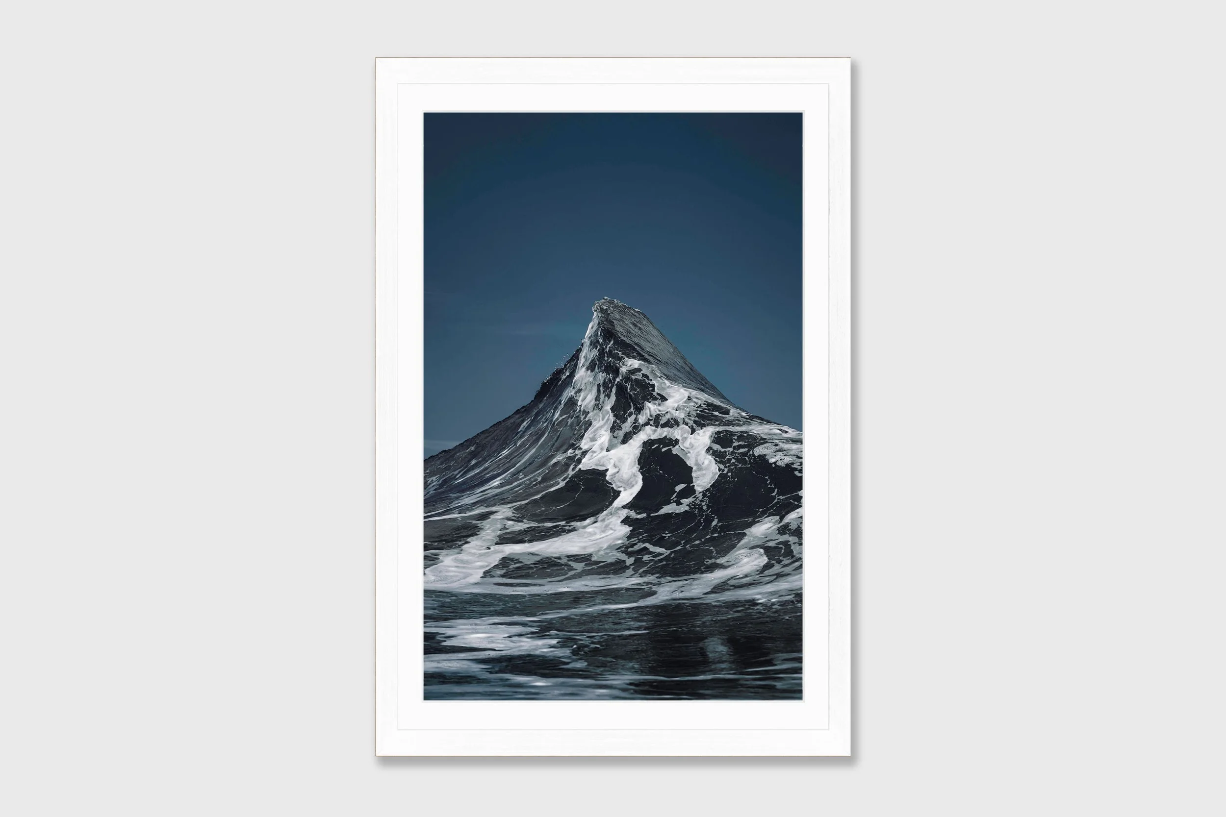 Two ocean waves crashing together forming a peak shape resembling the Matterhorn mountain, captured in dramatic coastal light.