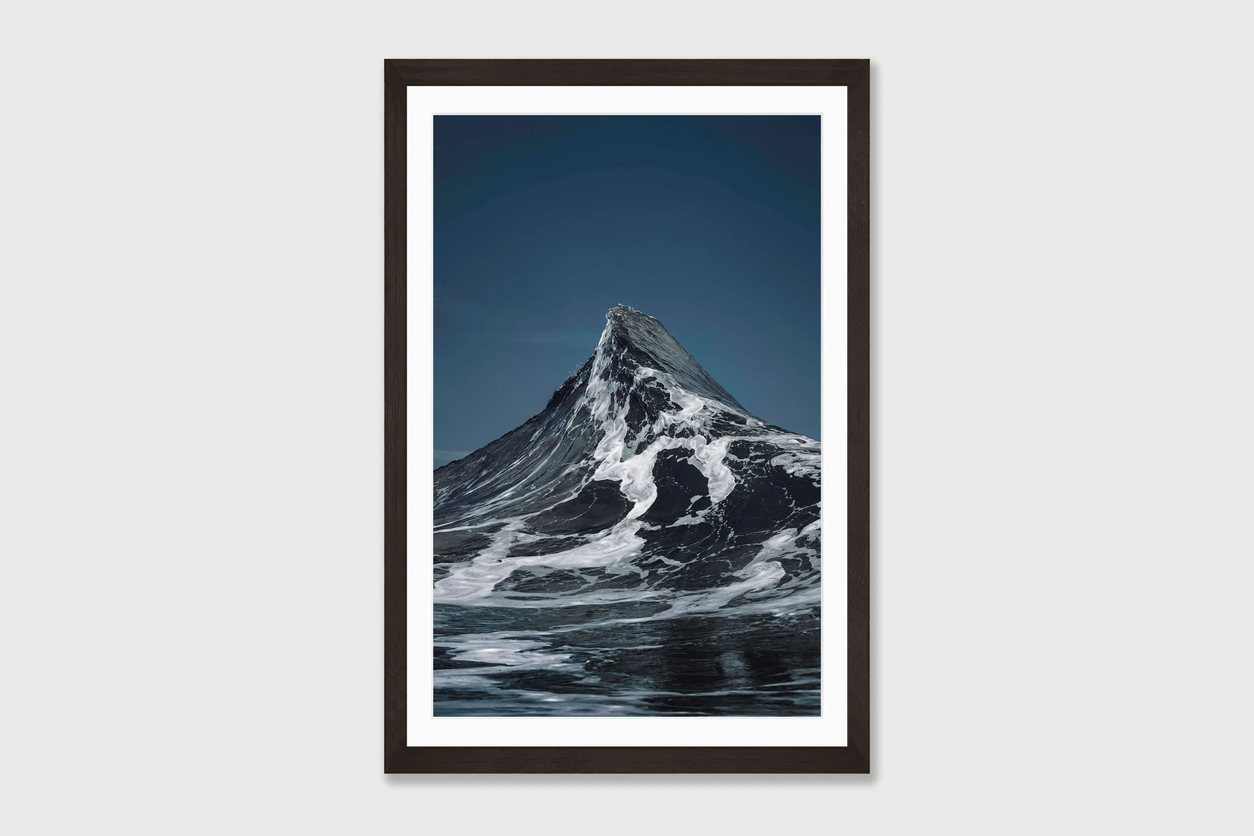 Two ocean waves crashing together forming a peak shape resembling the Matterhorn mountain, captured in dramatic coastal light.