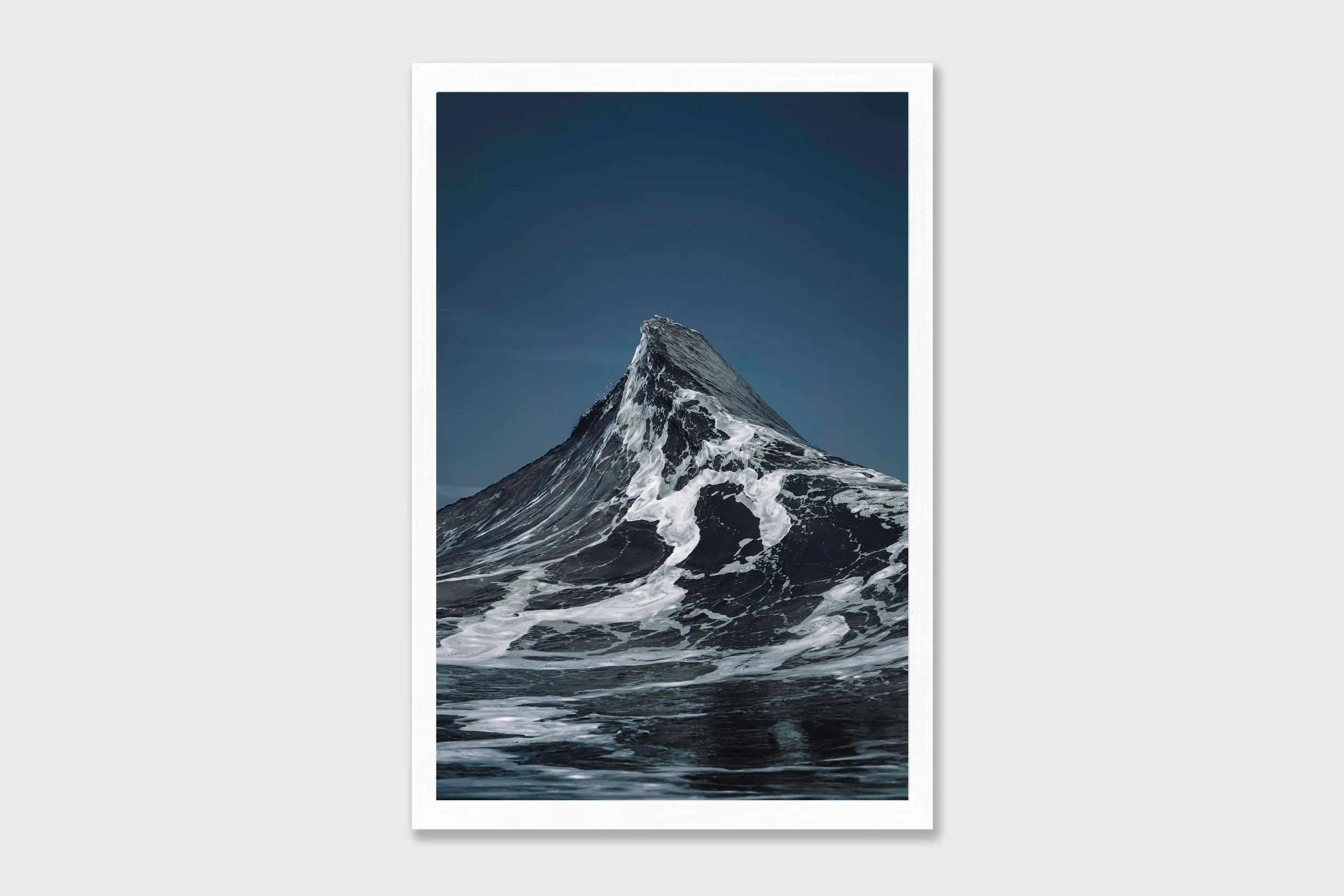 Two ocean waves crashing together forming a peak shape resembling the Matterhorn mountain, captured in dramatic coastal light.