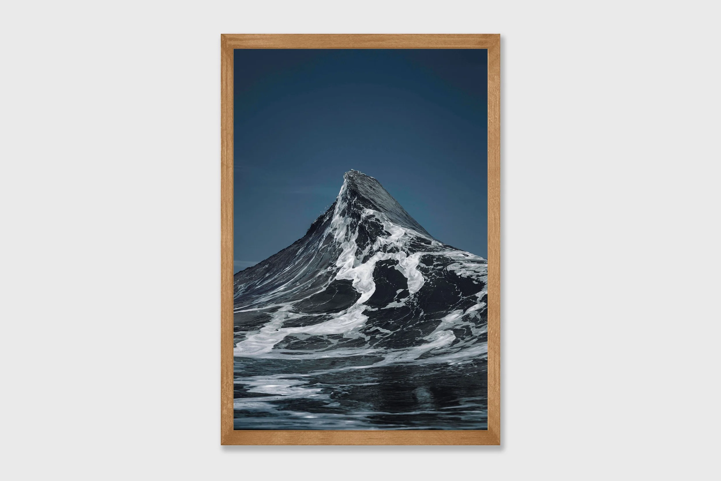 Two ocean waves crashing together forming a peak shape resembling the Matterhorn mountain, captured in dramatic coastal light.