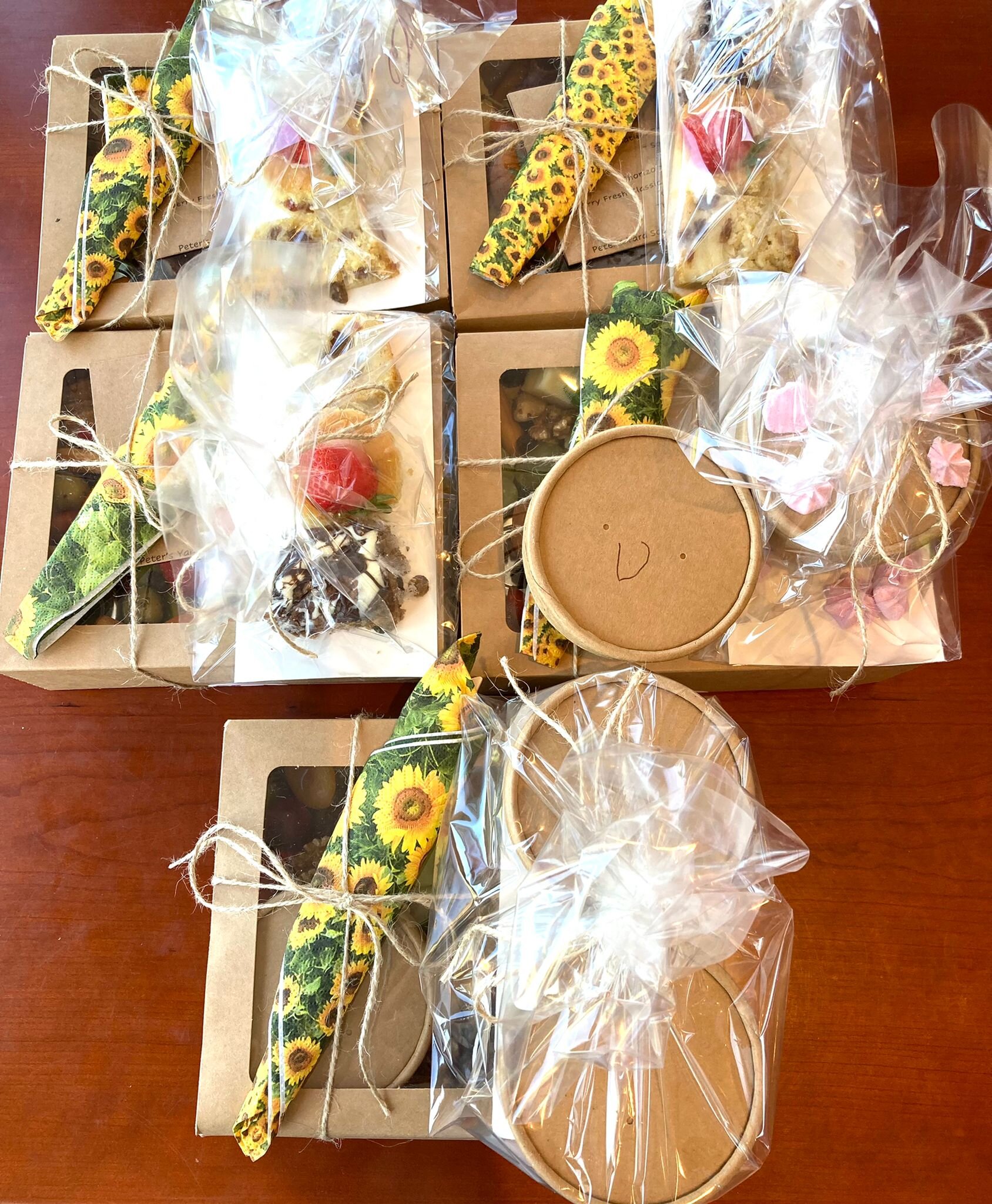 packaging of five grazing boxes with puddings of cakes or yogurt and fruit. knives forks and spoons wrapped in a serviette