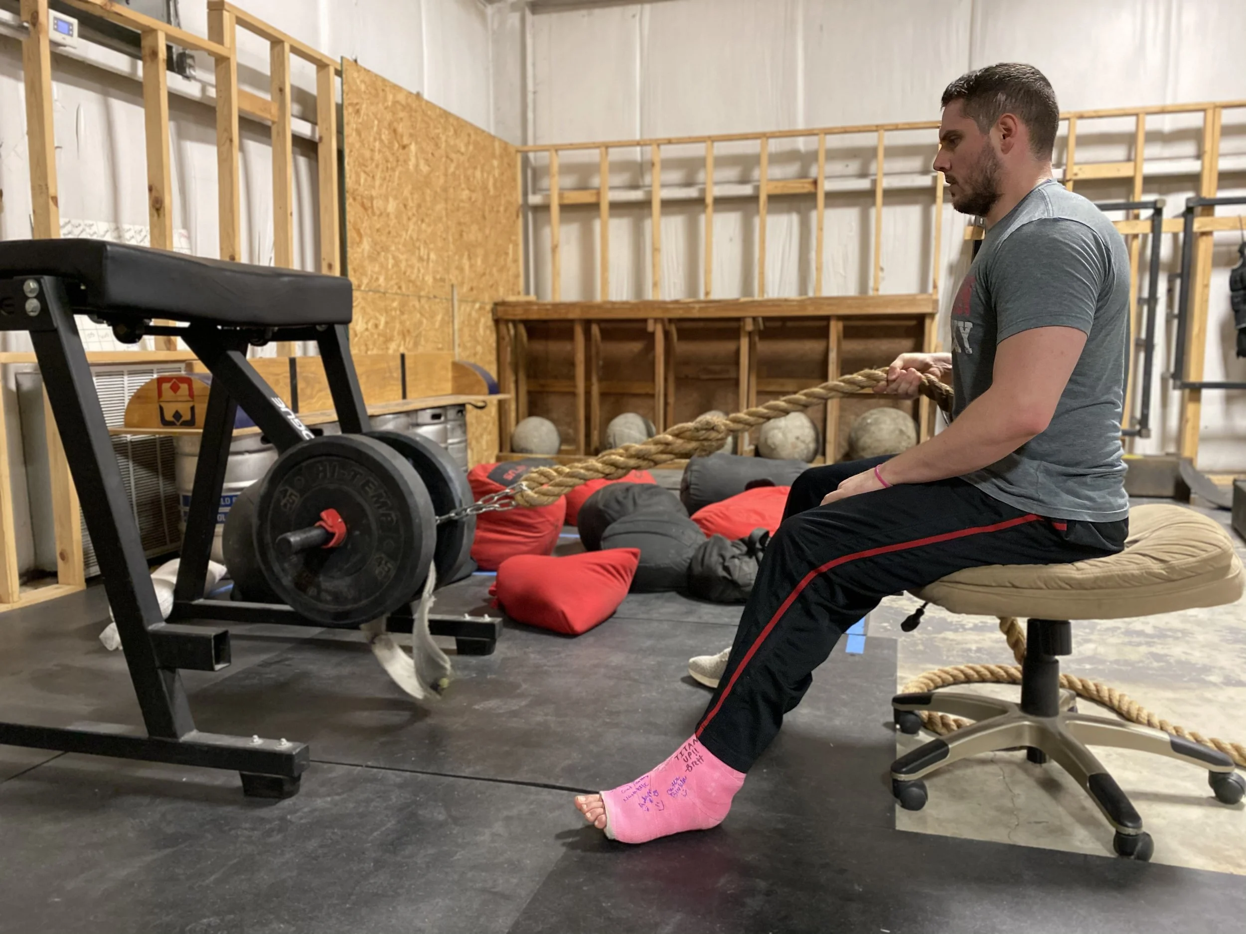 a man with a cast on his ankle doing a seated row with a rope
