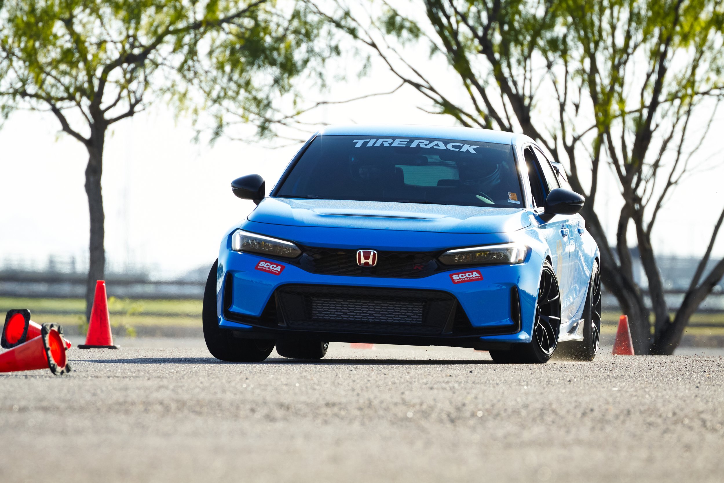 Blue Honda Civic Type R parked on a paved surface with orange cones and trees in the background.