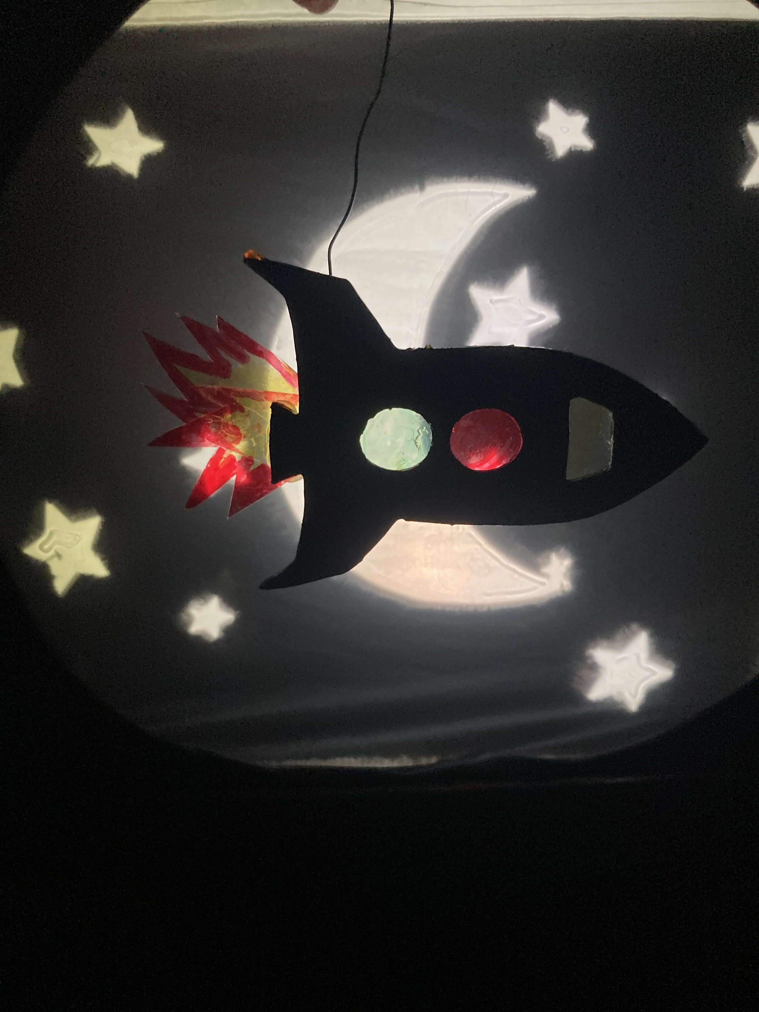 Alt Text:A puppet rocket flies past a shadow star and moon scene 