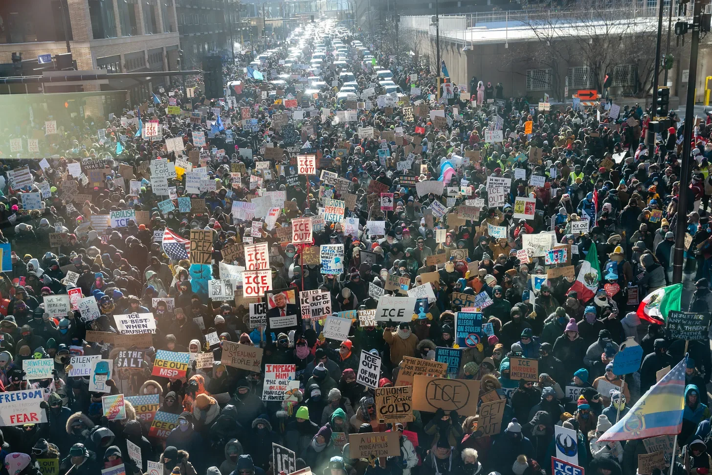 A large crowd marches down a city street, holding signs and flags in support of immigrant rights.