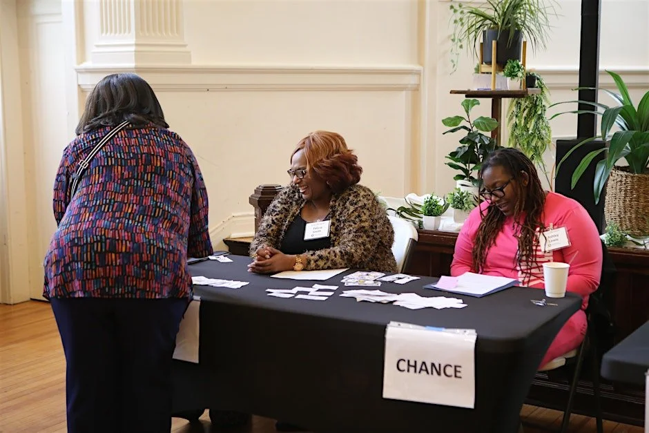 Two women sitting at a registration table assisting another woman with the registration process