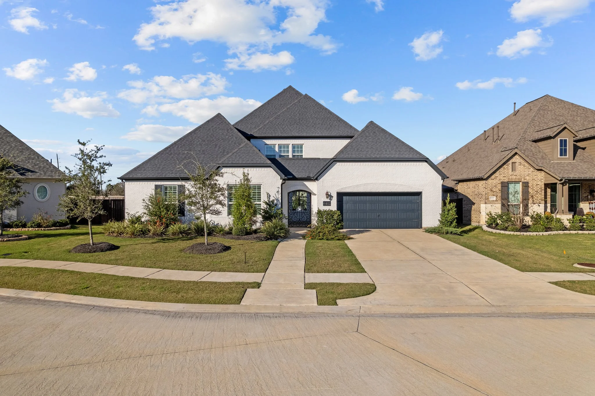 Front view of a modern two-story house with a white exterior, black roof, black garage door, and small front yard with landscaping.