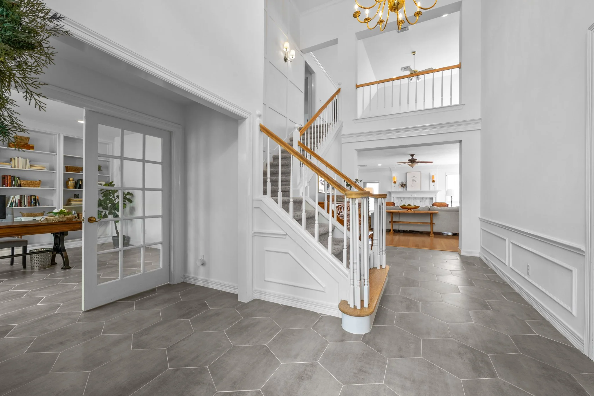 Interior of a house with a staircase, white walls, tile flooring, and a chandelier hanging from the ceiling.