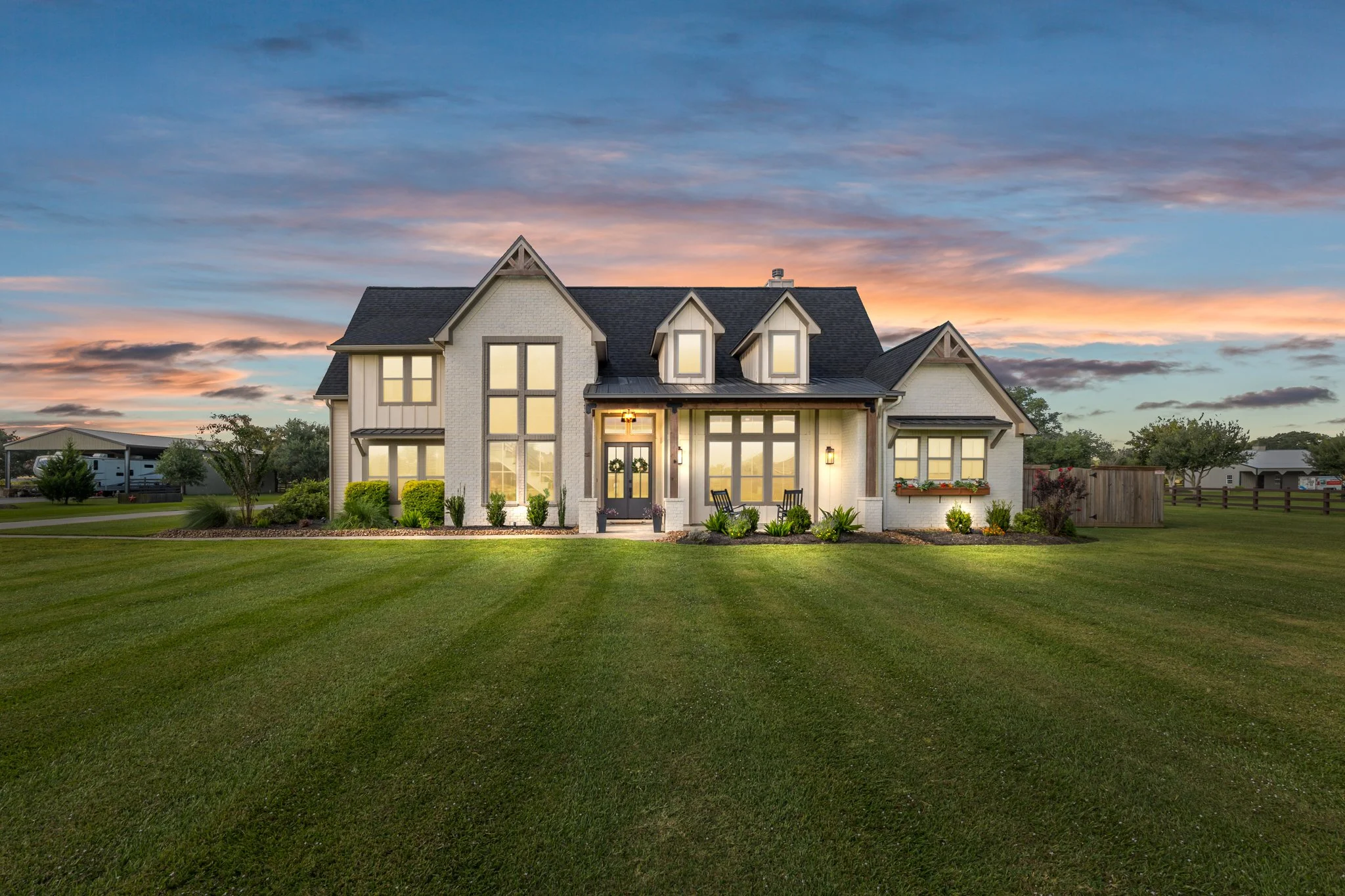 A large modern house with white exterior walls and dark roof, surrounded by a well-manicured lawn at sunset.