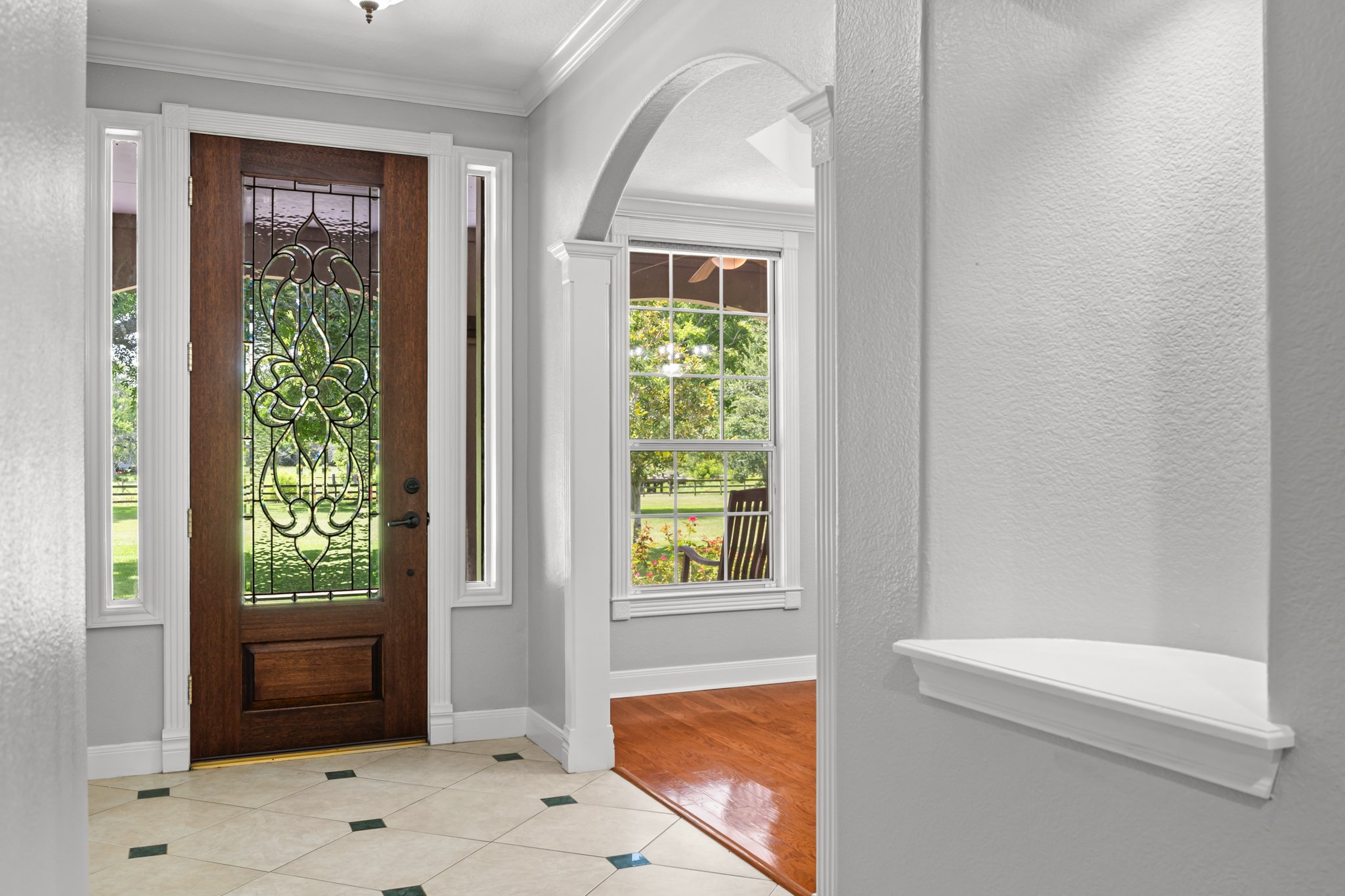 Entryway with a wooden front door featuring decorative glass, a window and a view of a garden and porch outside.