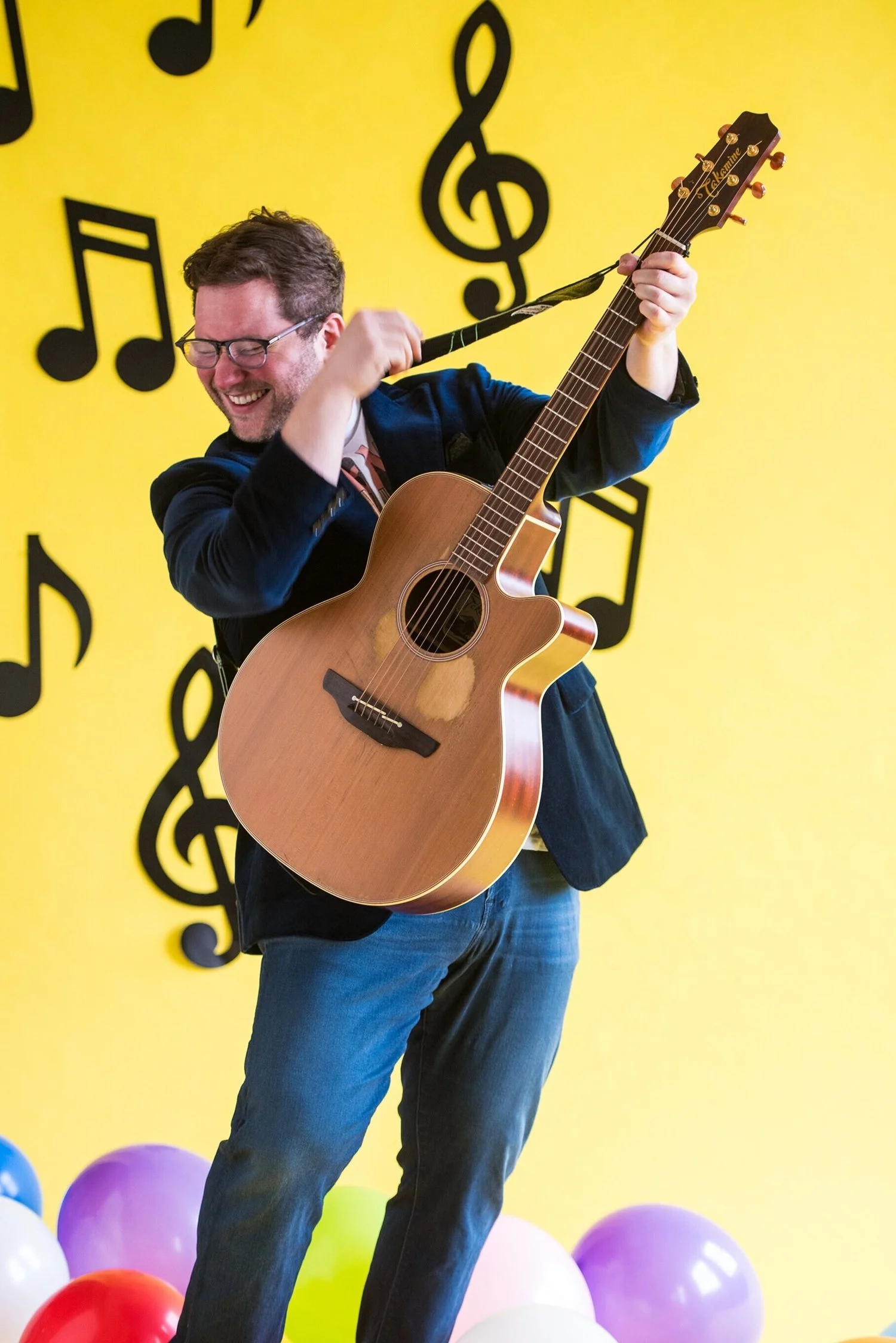 Jesse Jukebox holding his guitar against a bright yellow musical backdrop