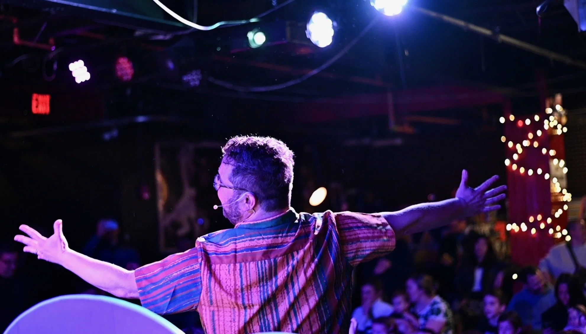 Jesse Jukebox onstage with arms outstretched, facing a family audience under colorful concert lights