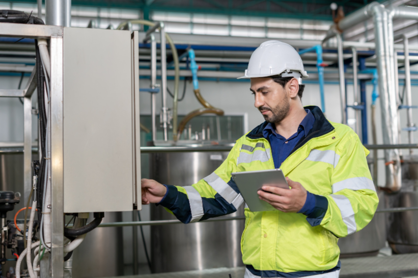 A man in a white safety helmet and neon yellow safety jacket working with industrial equipment in a factory.