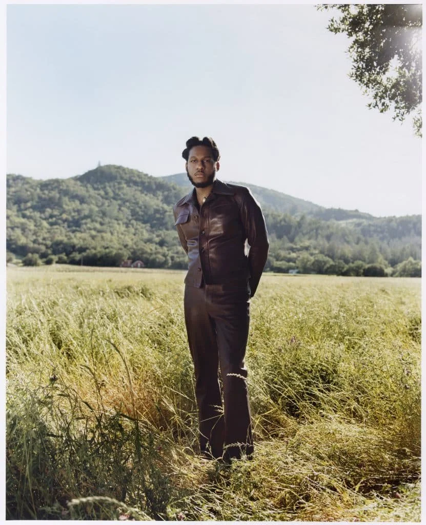 portrait of musician leon bridges wearing brown leather suit in a field